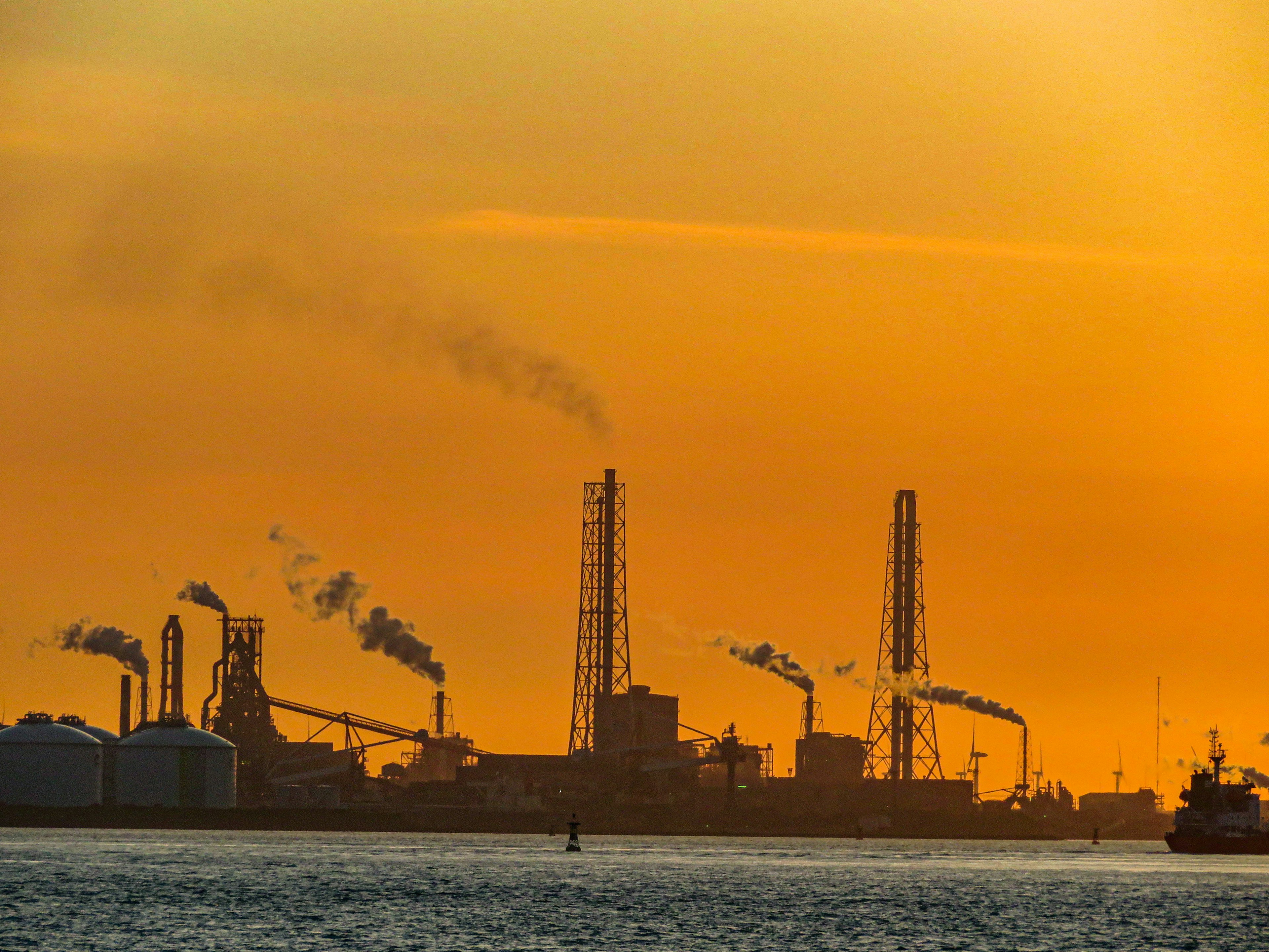 Silhouette of an industrial area against a sunset featuring smokestacks and storage tanks