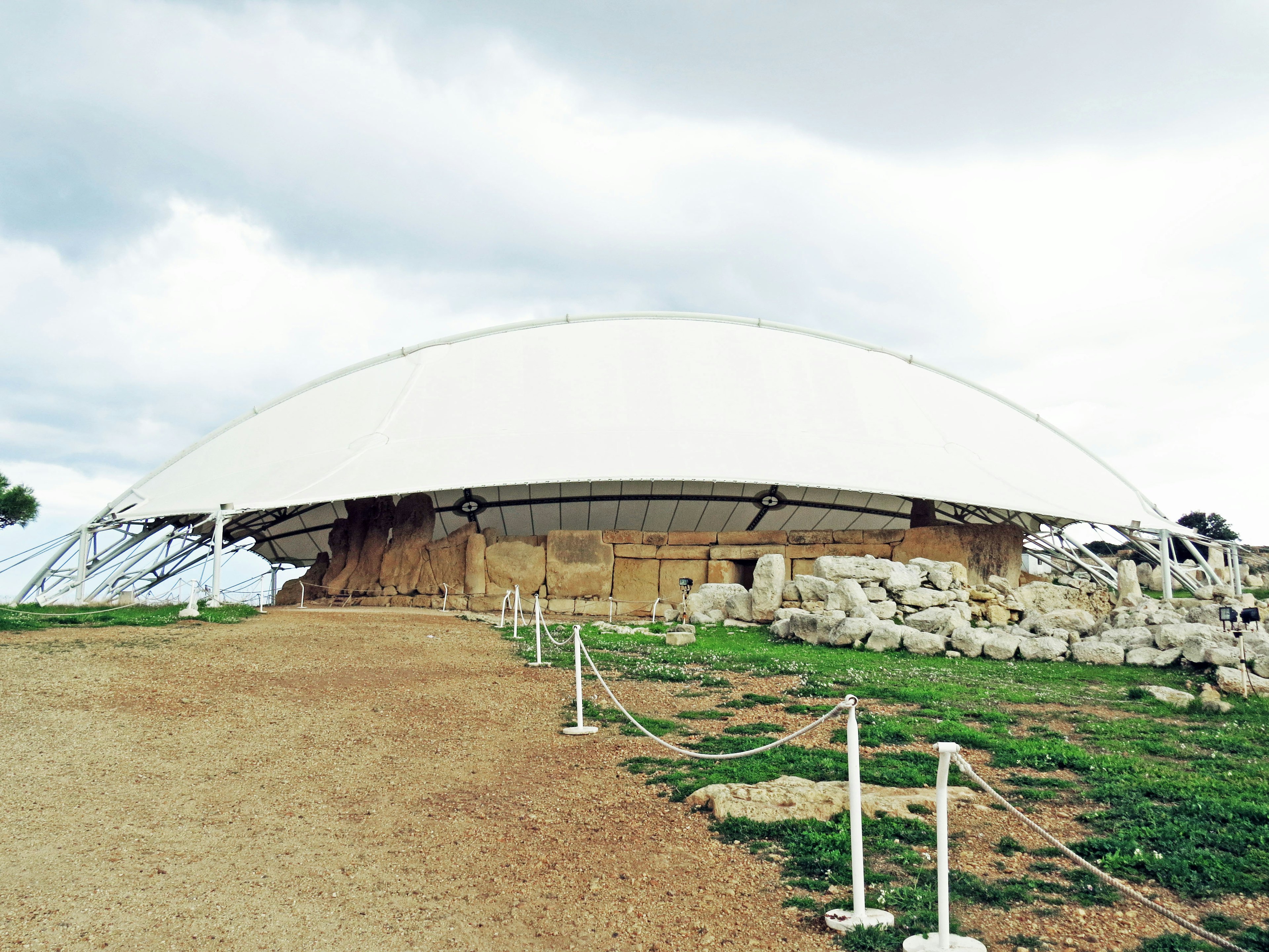 Estructura de cúpula blanca que cubre ruinas antiguas rodeadas de hierba verde