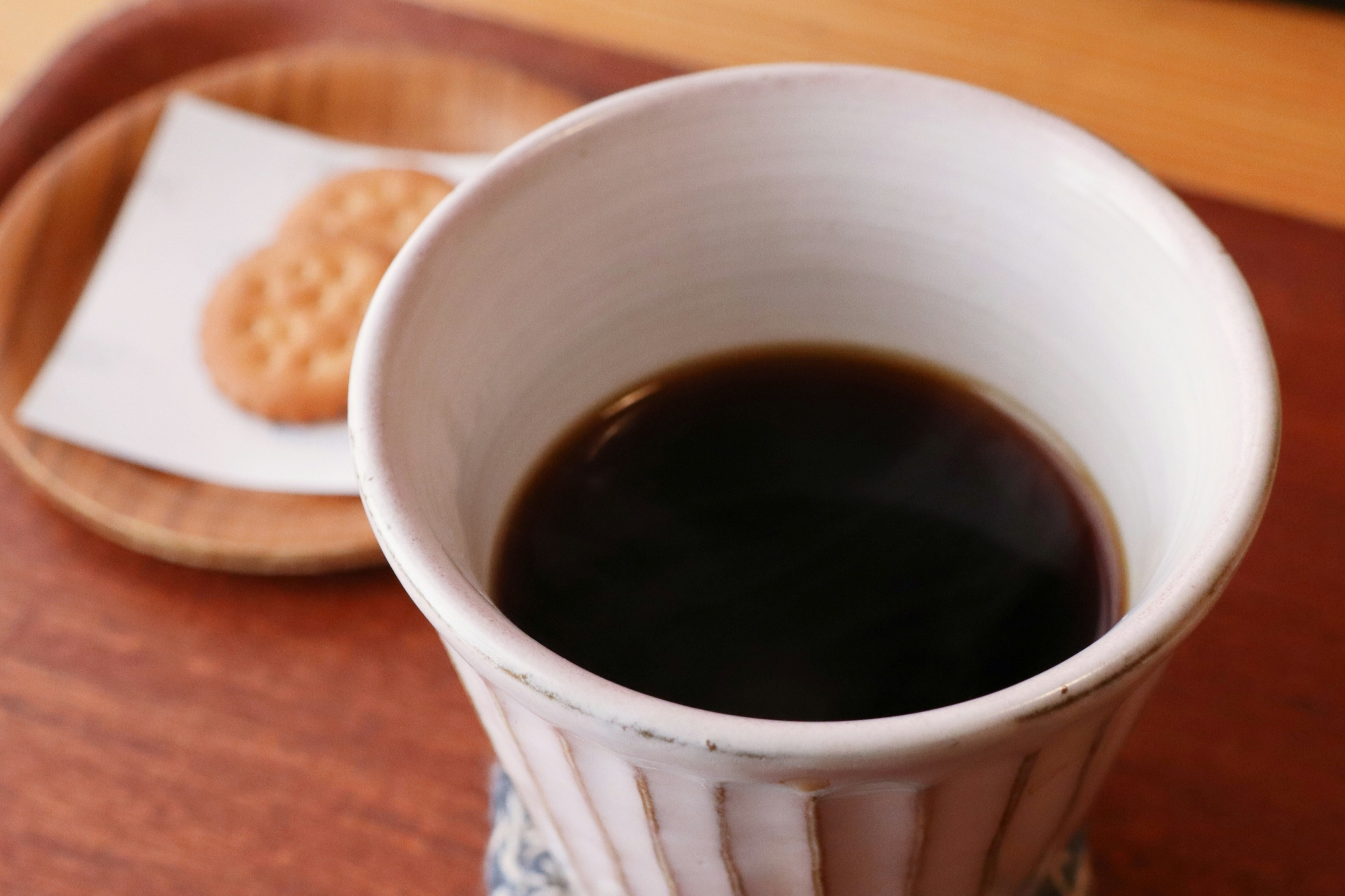 Una imagen acogedora con una taza de café negro y una galleta en una bandeja de madera