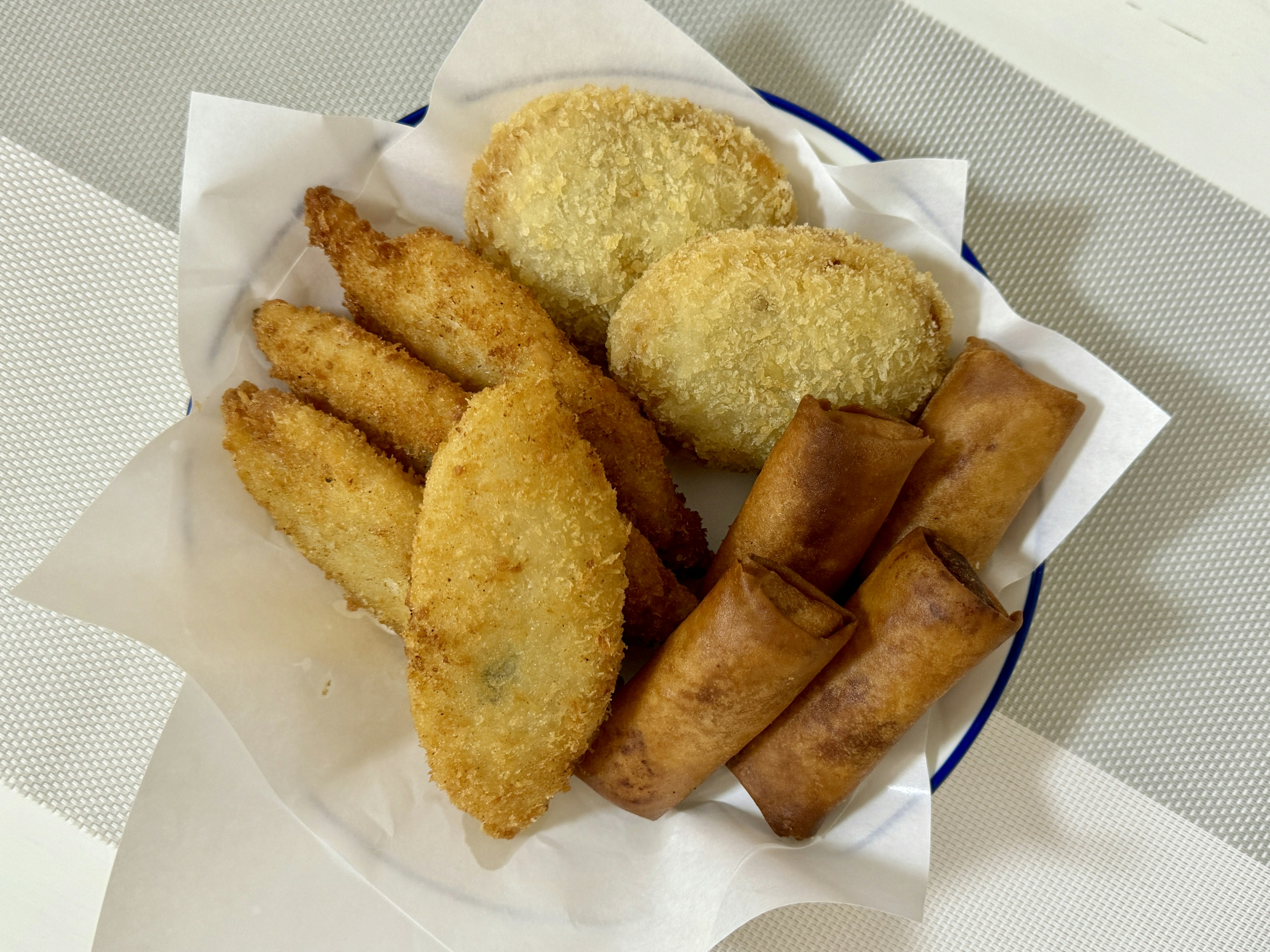 Una bandeja de alimentos fritos variados que incluye croquetas y rollos de primavera