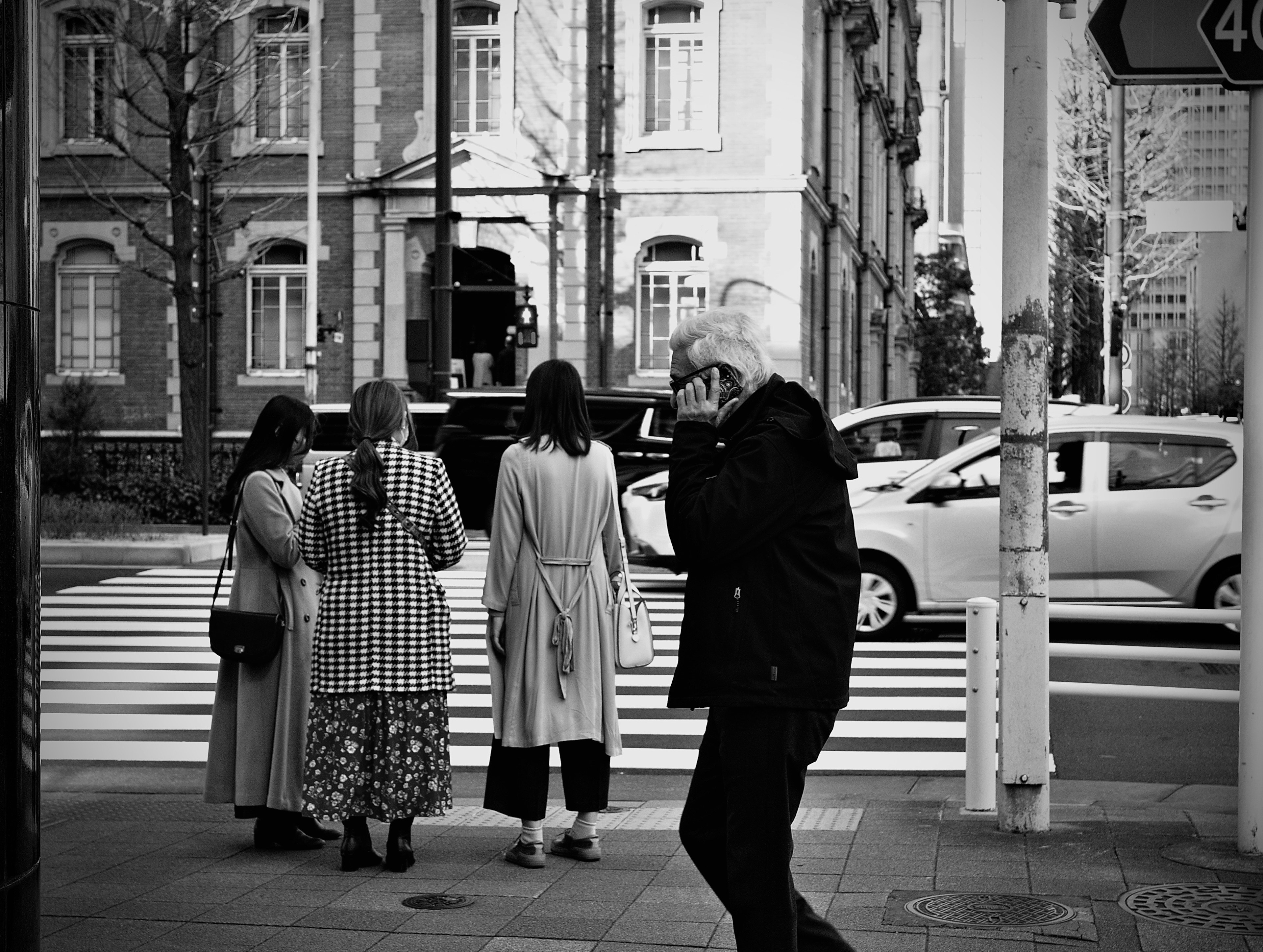 Black and white street scene with women waiting at a crosswalk and a passerby