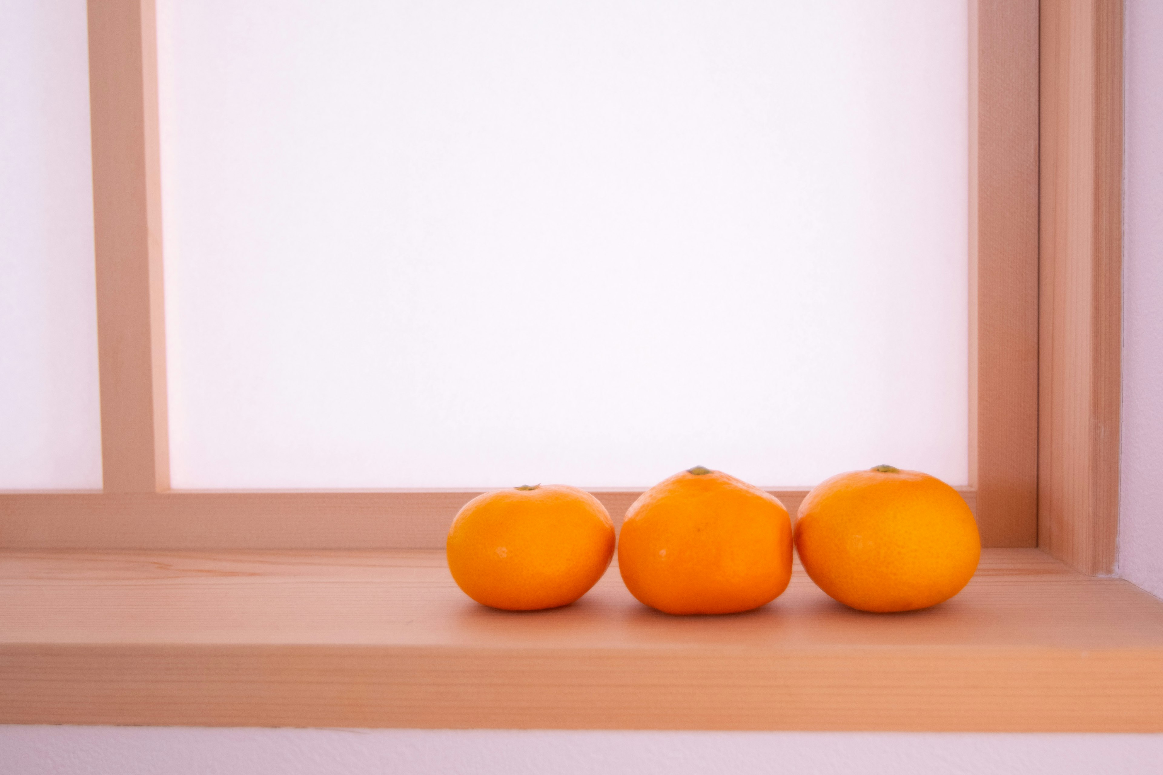 Three orange fruits placed on a wooden windowsill