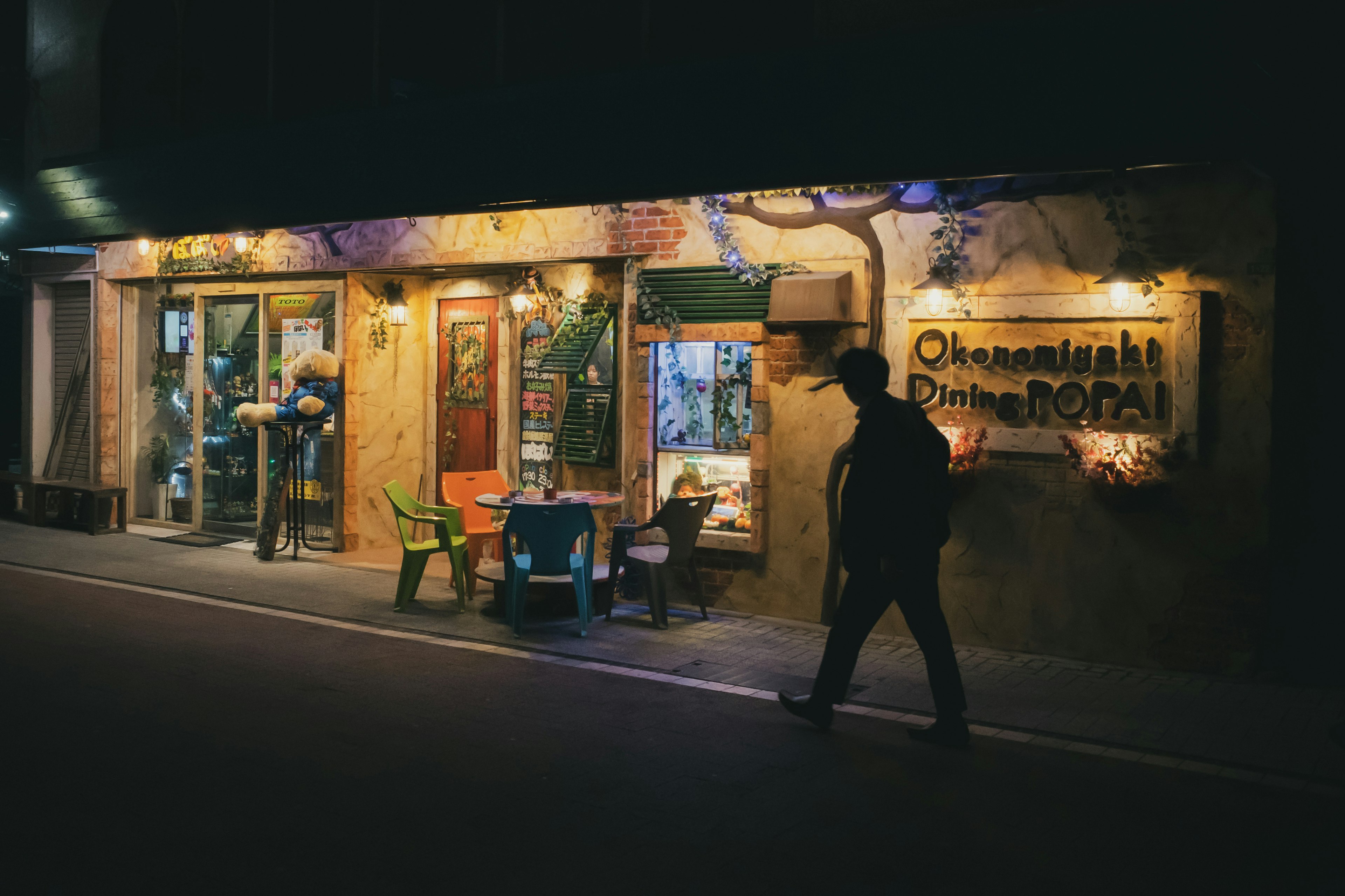 Fachada colorida de una tienda de noche con una persona caminando