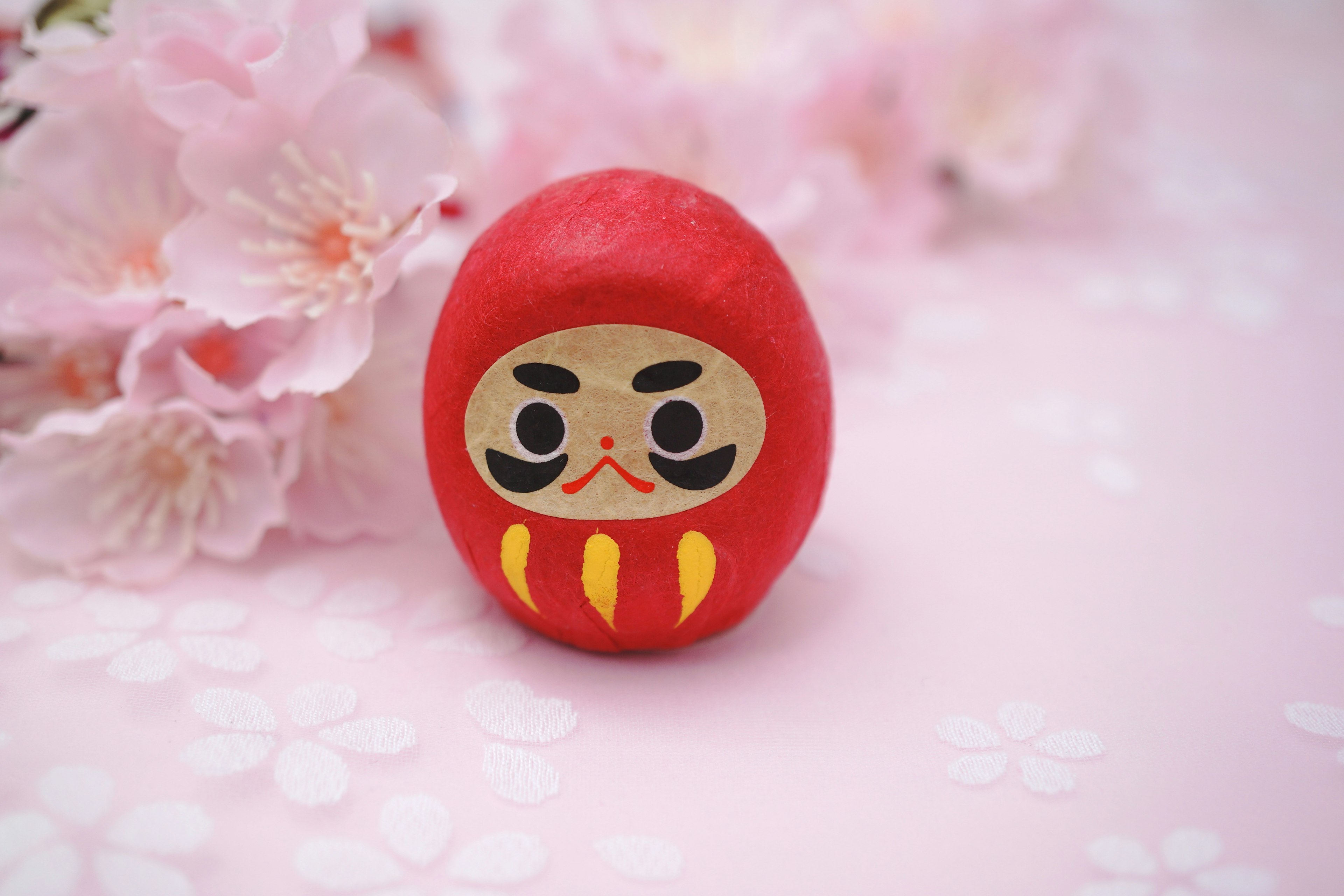 Boneka Daruma merah yang diletakkan di atas kelopak bunga sakura