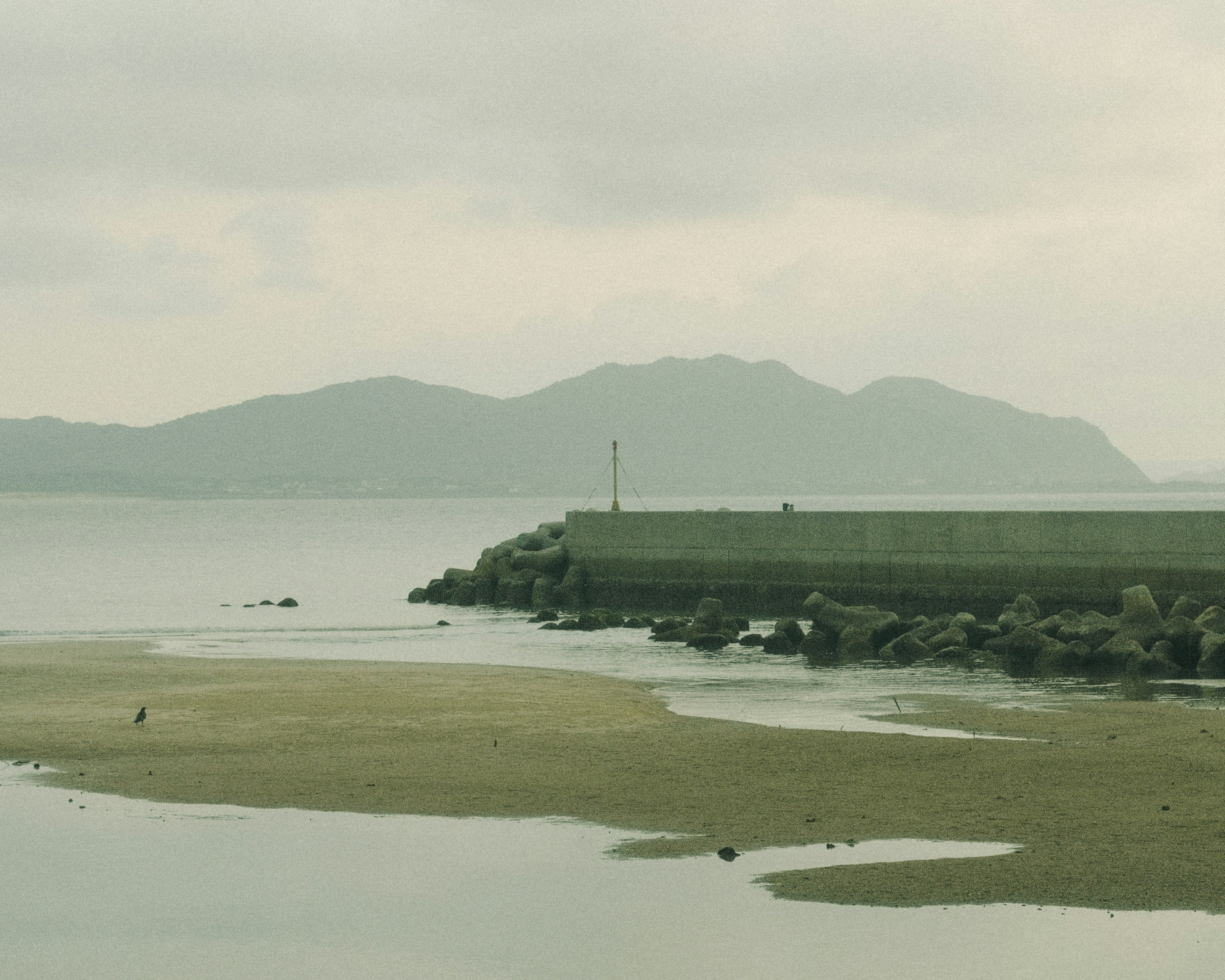 Scenic view of a breakwater with distant mountains on a cloudy day