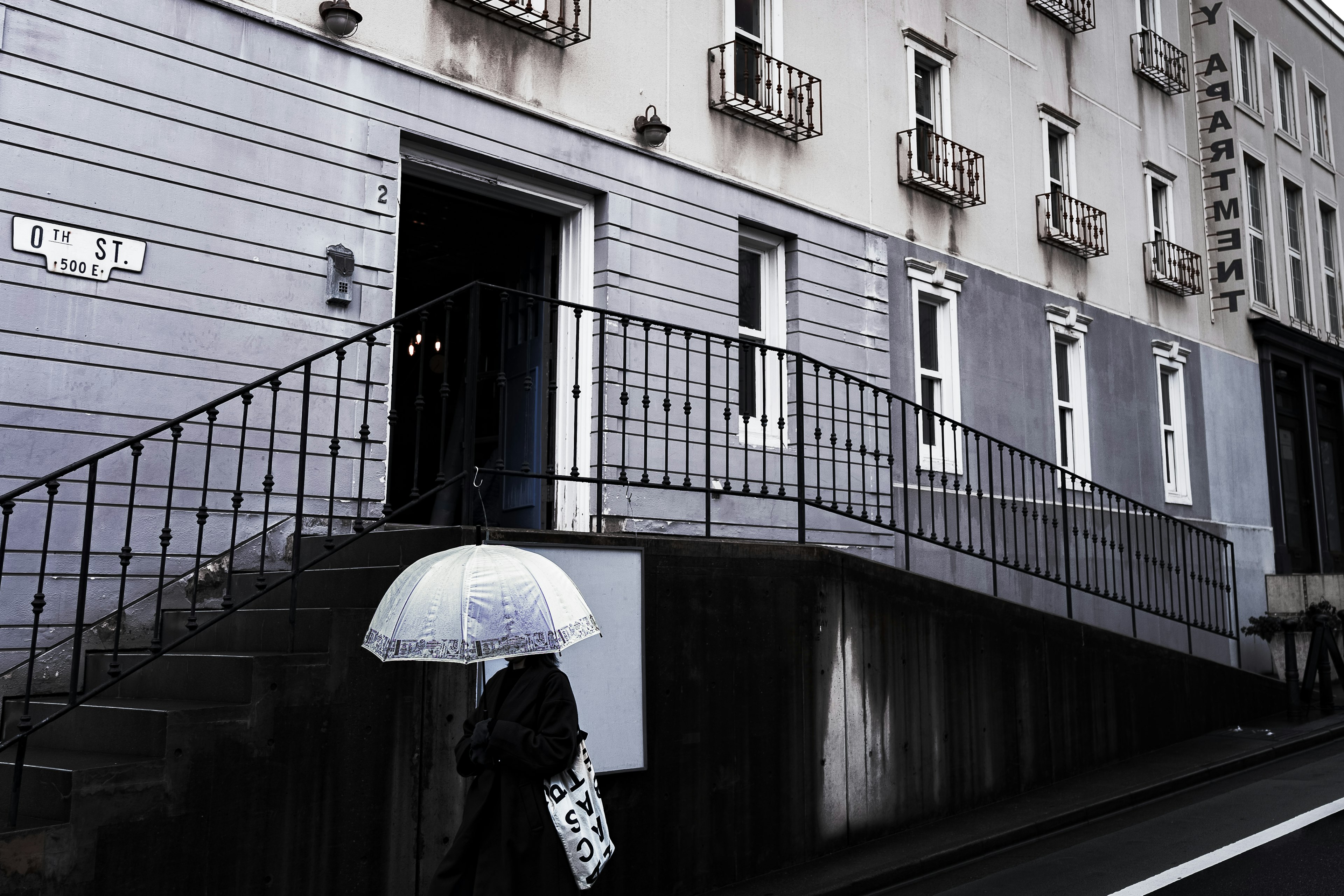 A person walking in front of a gray building holding a white umbrella