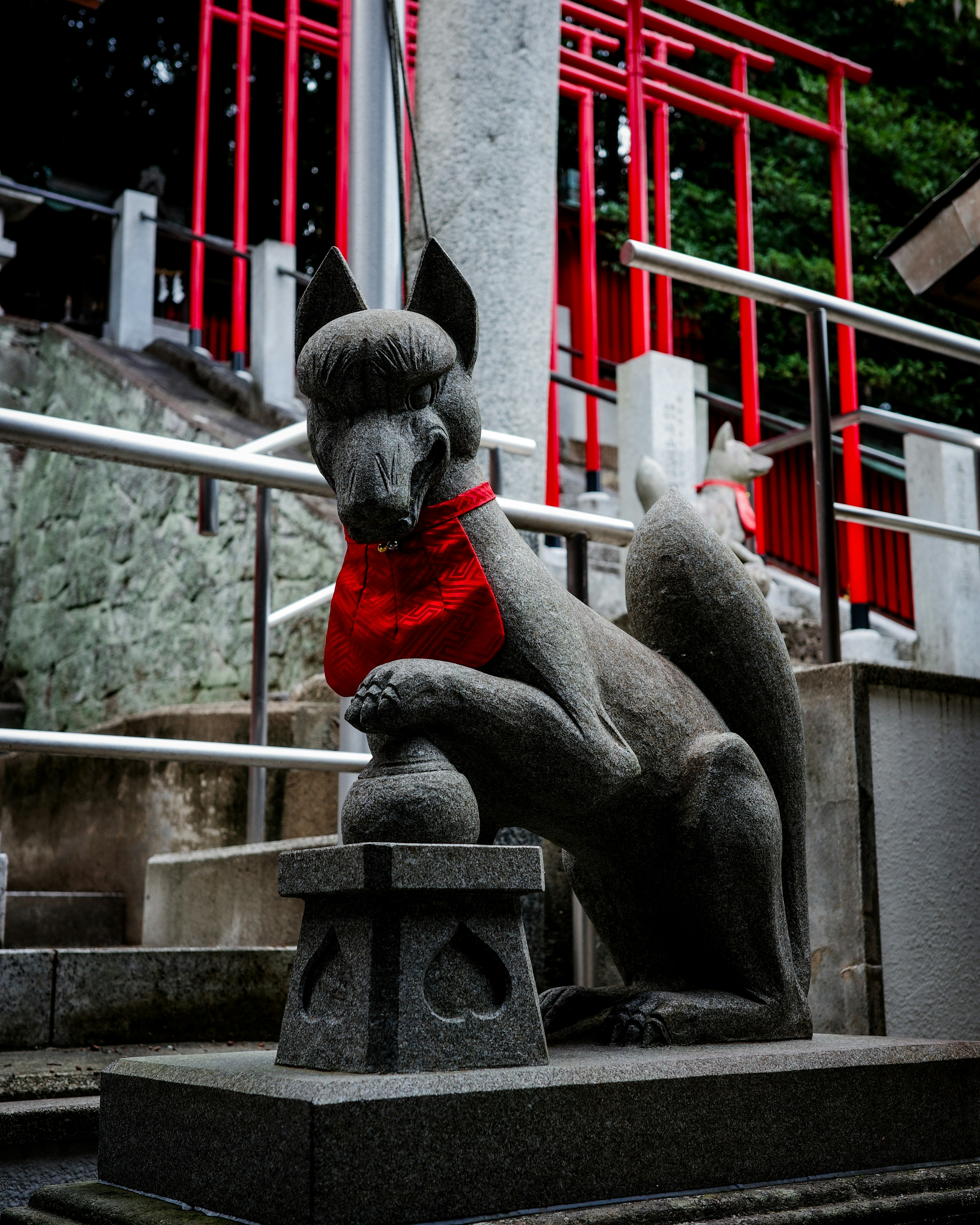 赤いスカーフをつけた狐の石像が神社の階段に立っている