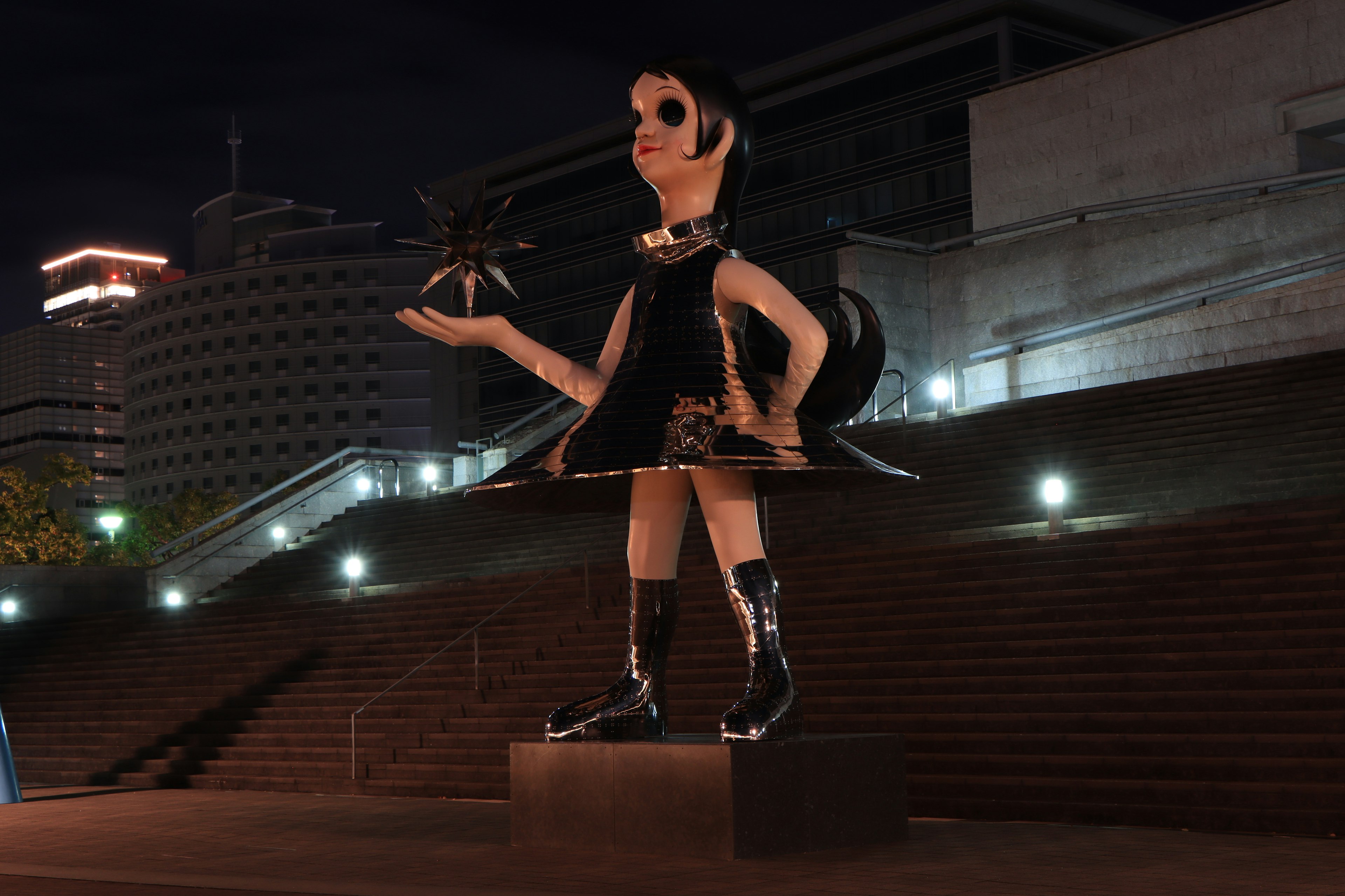 Large character statue in a city at night A woman in black clothing holding a small object