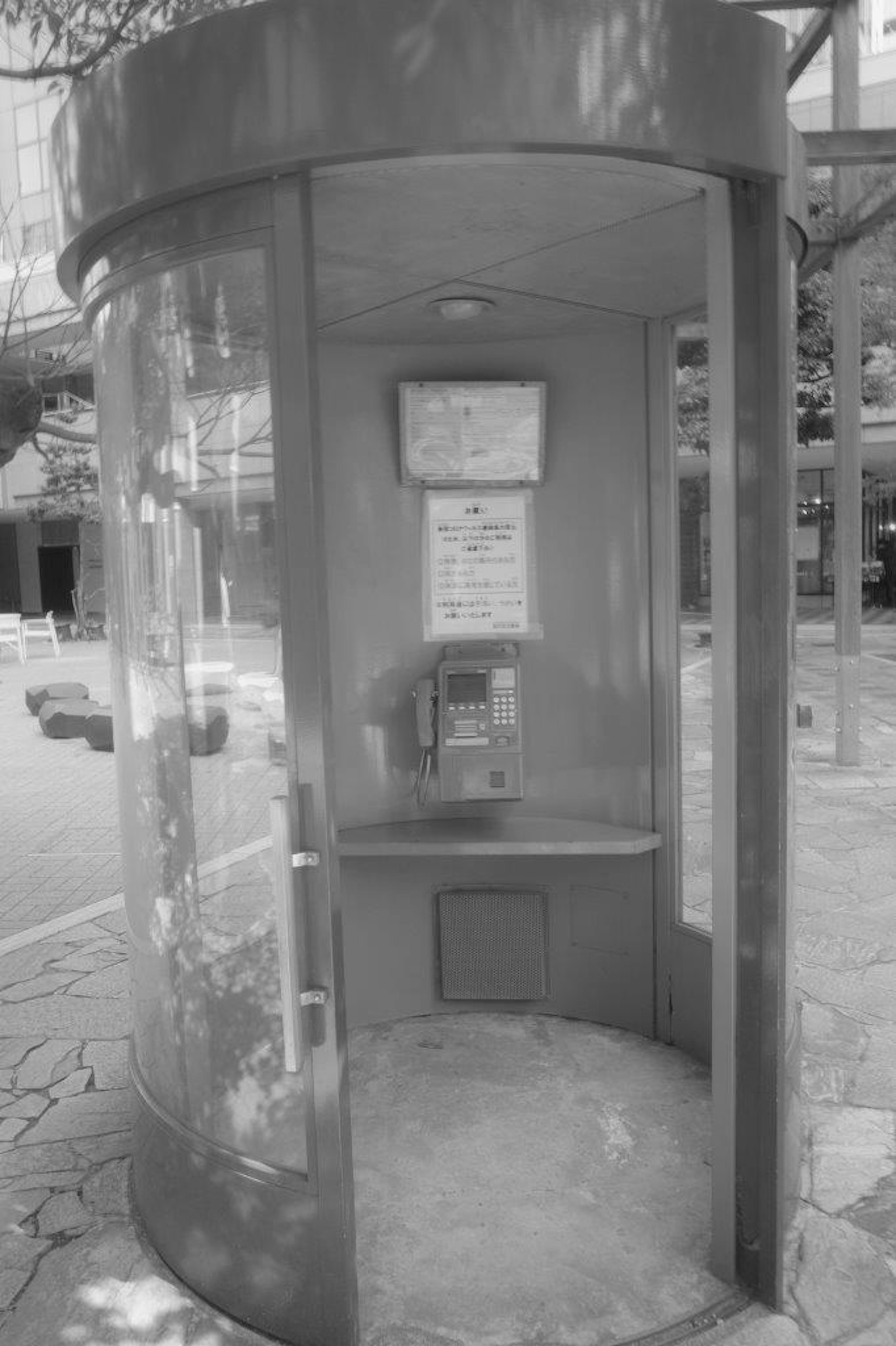 Interior of a public telephone booth with transparent walls and round shape featuring a payphone and notice board