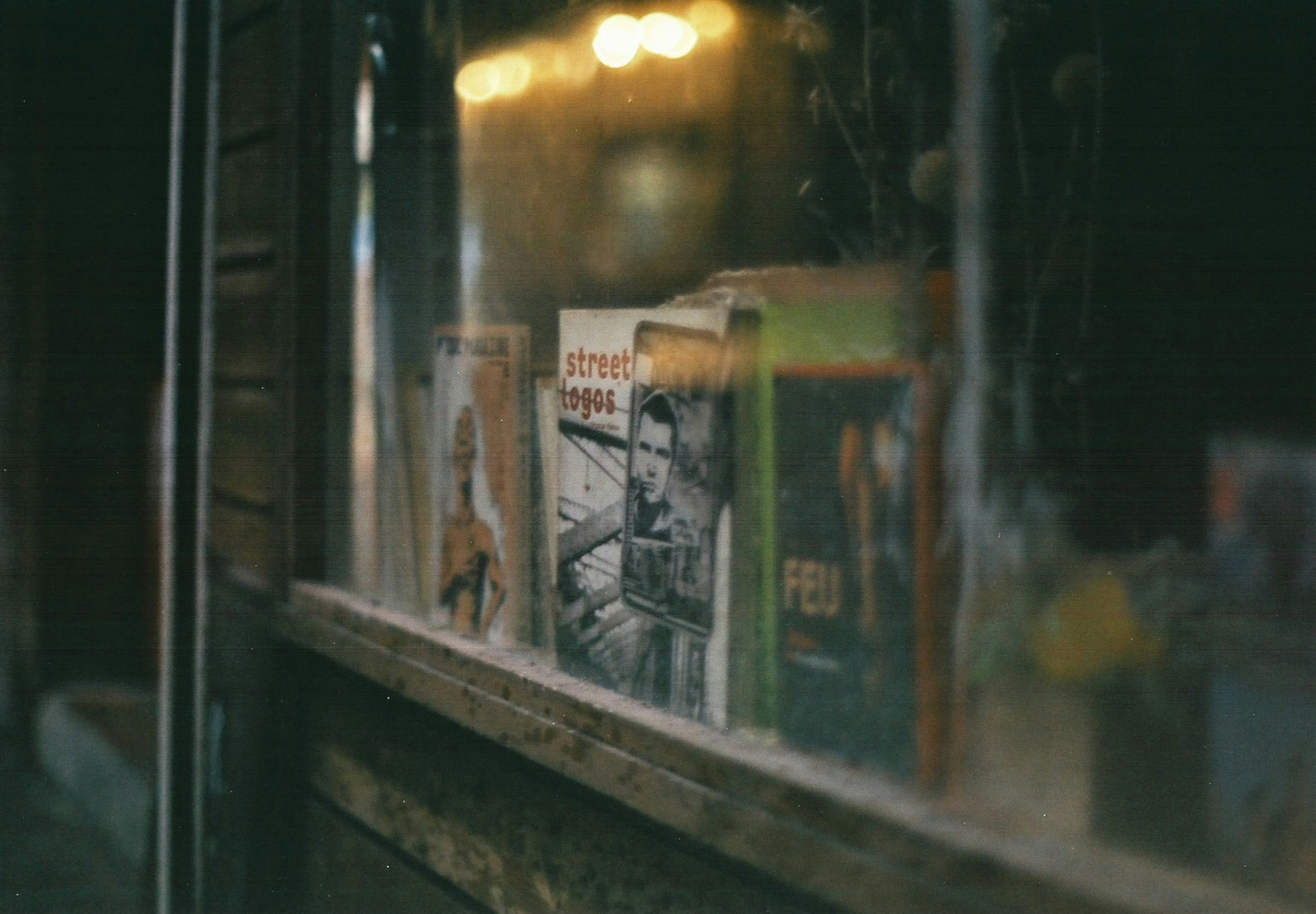 Blurred view of old magazines displayed in a window with street lights in the background