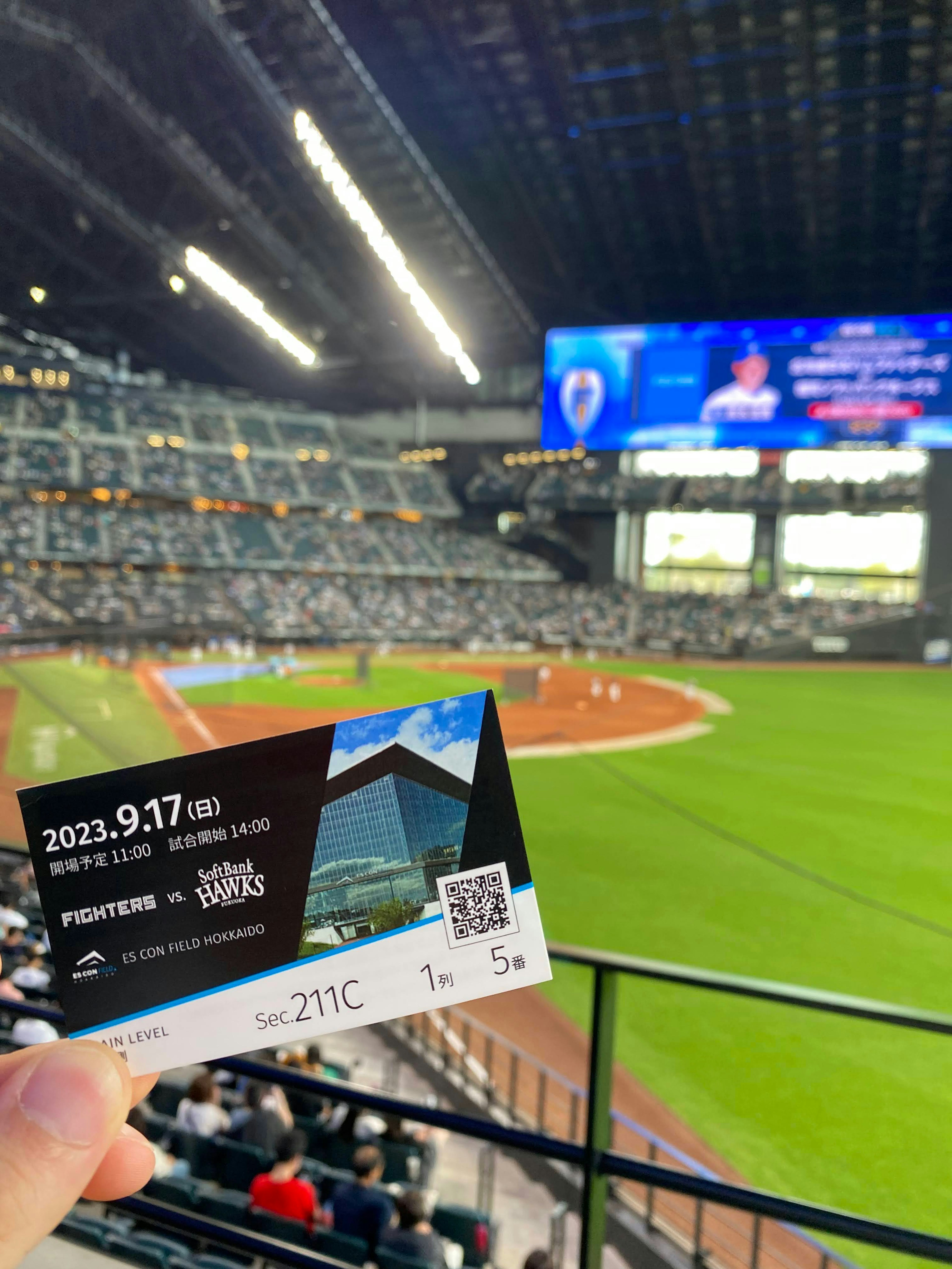 Espectador sosteniendo un boleto del estadio con un juego de béisbol a la vista