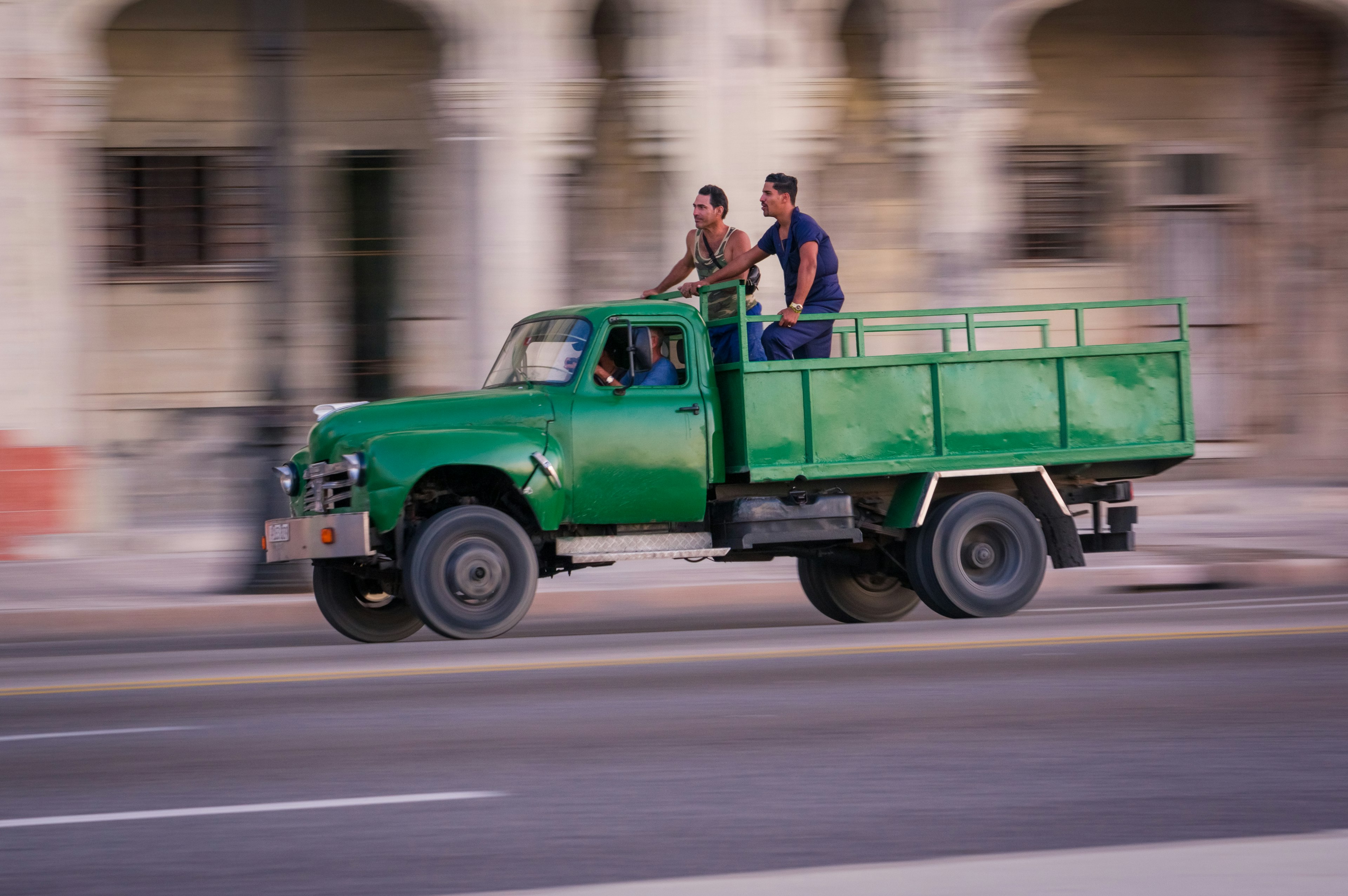 Two men riding on a green truck speeding down the street