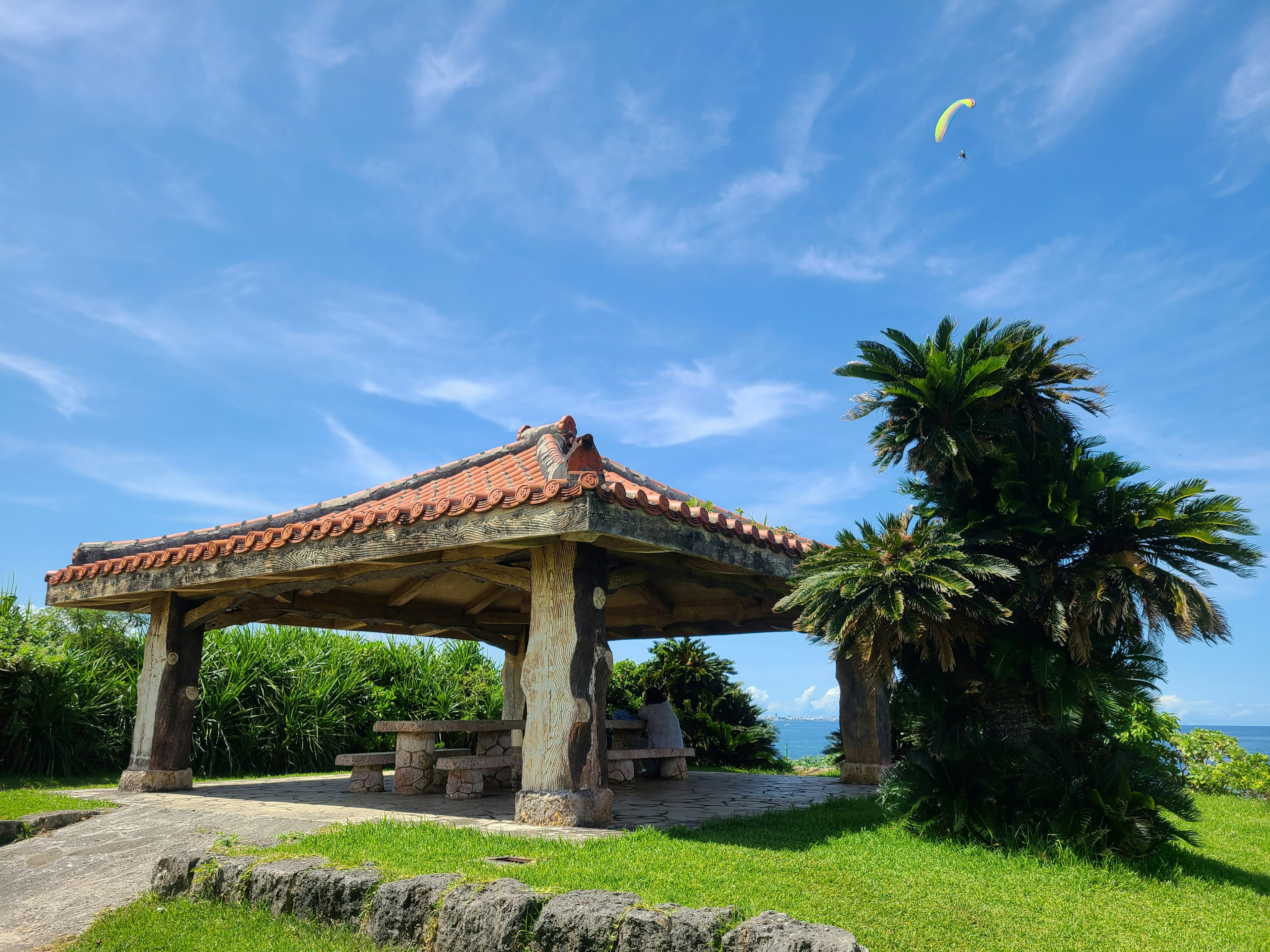 Pavillon traditionnel d'Okinawa sous un ciel bleu entouré de pelouse verte et de palmiers