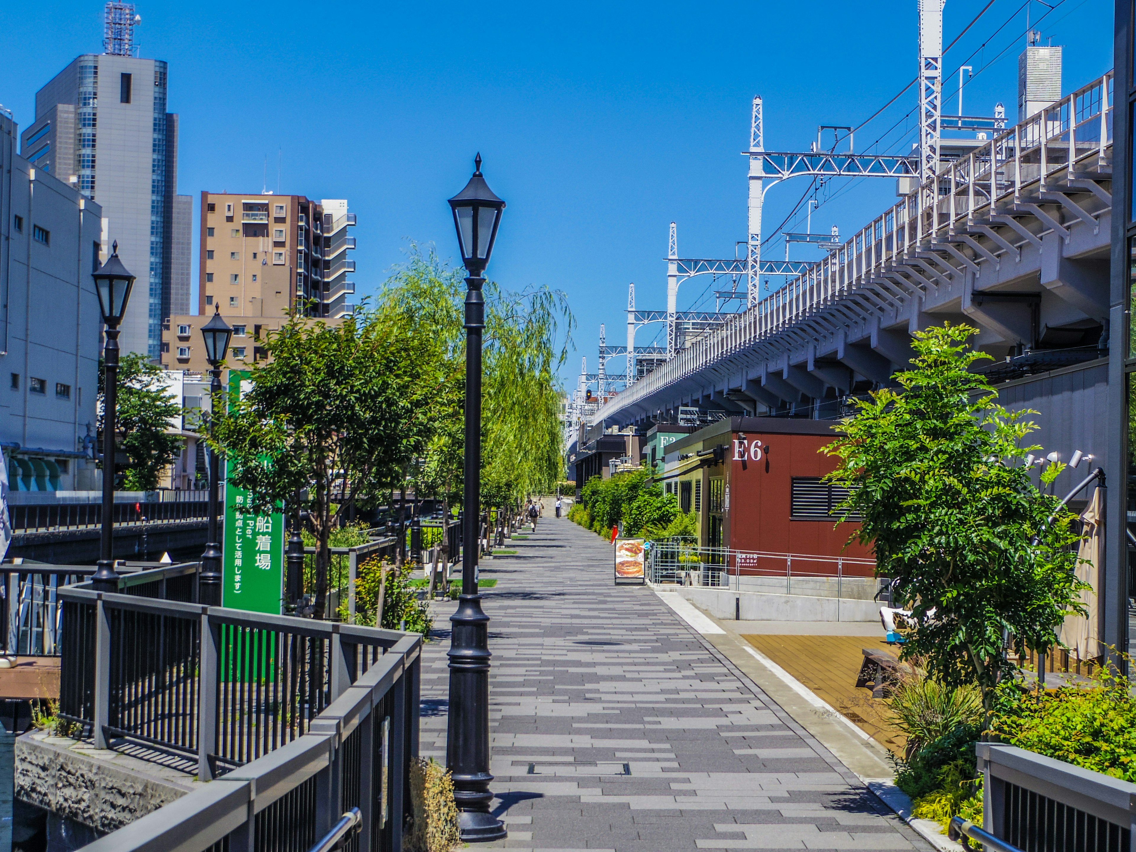 Parkweg unter blauem Himmel mit sichtbaren Straßenlaternen und Bahngleisen