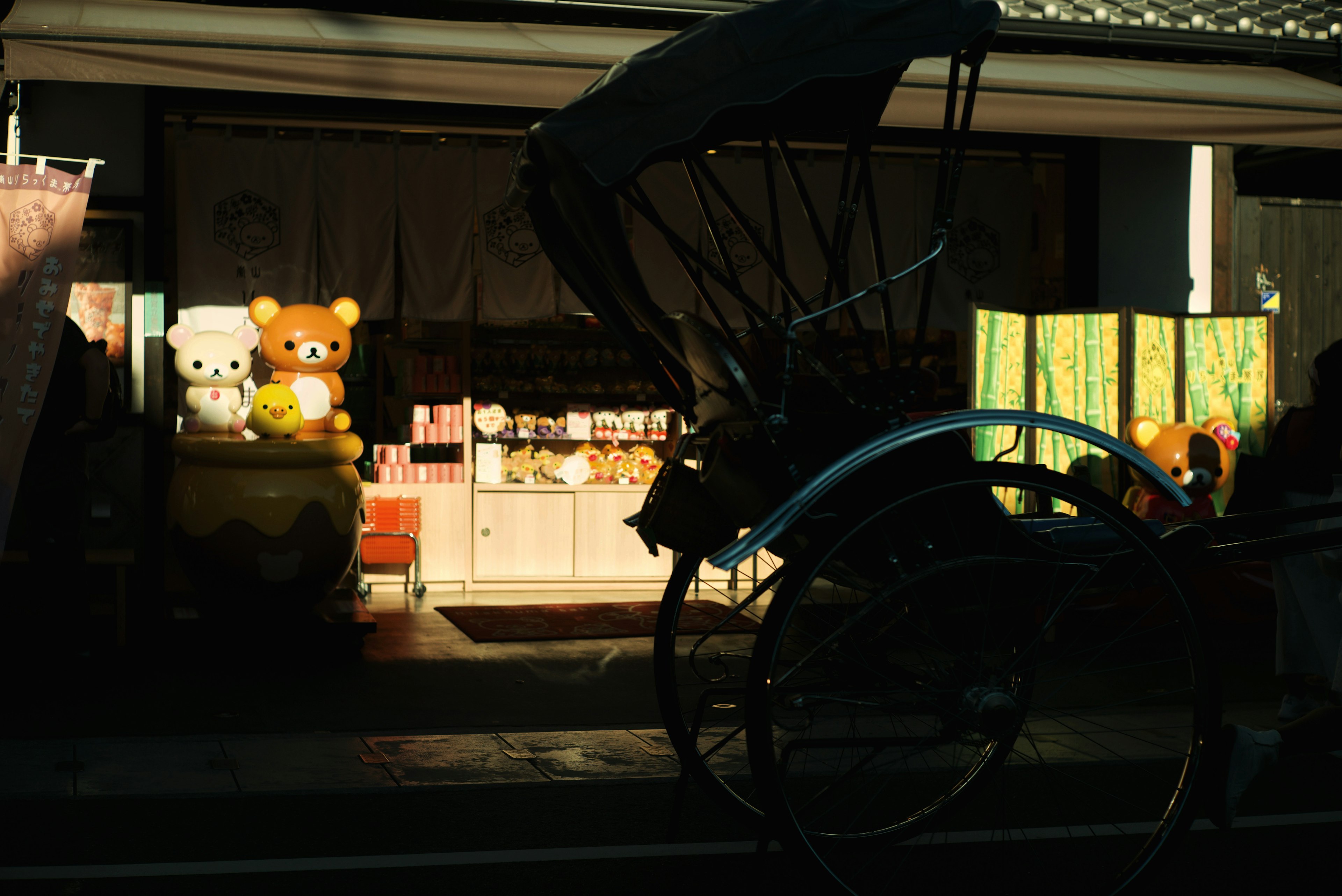 Vitrina de tienda con peluches Rilakkuma y Korilakkuma y un rickshaw en primer plano