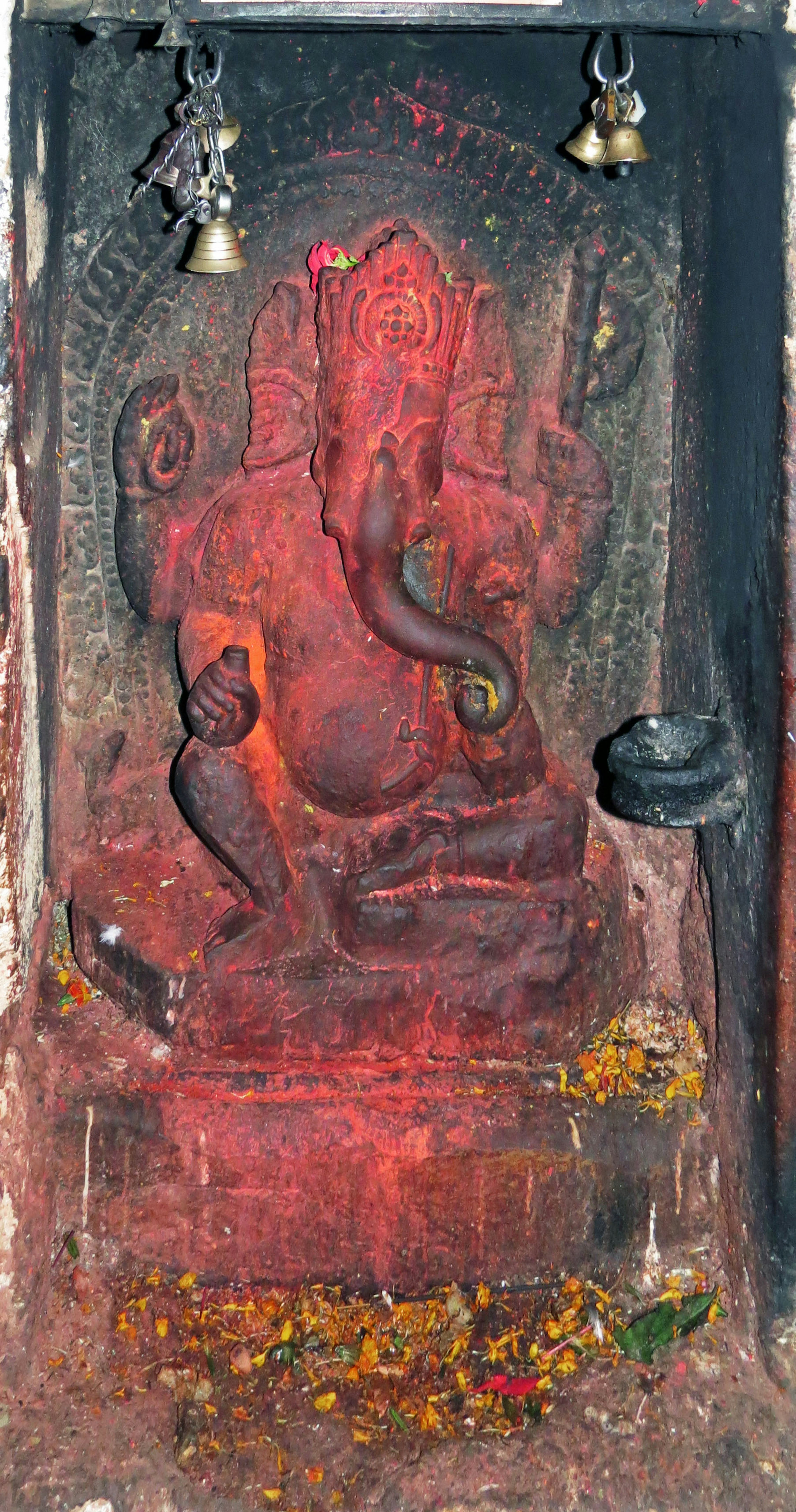 Red Ganesh statue on an altar surrounded by flower petals and an incense holder