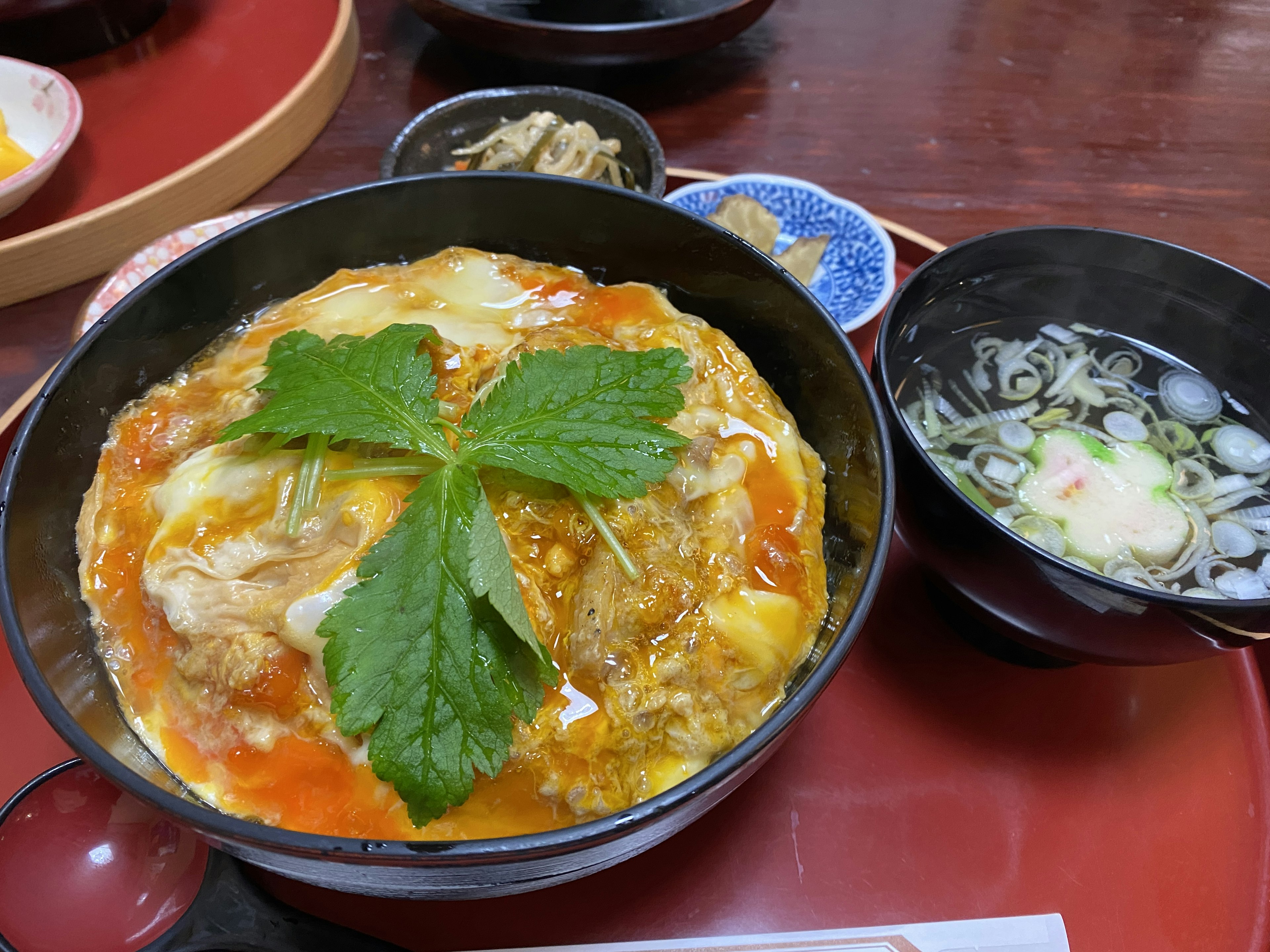 A bowl of oyakodon topped with green leaves alongside a bowl of miso soup