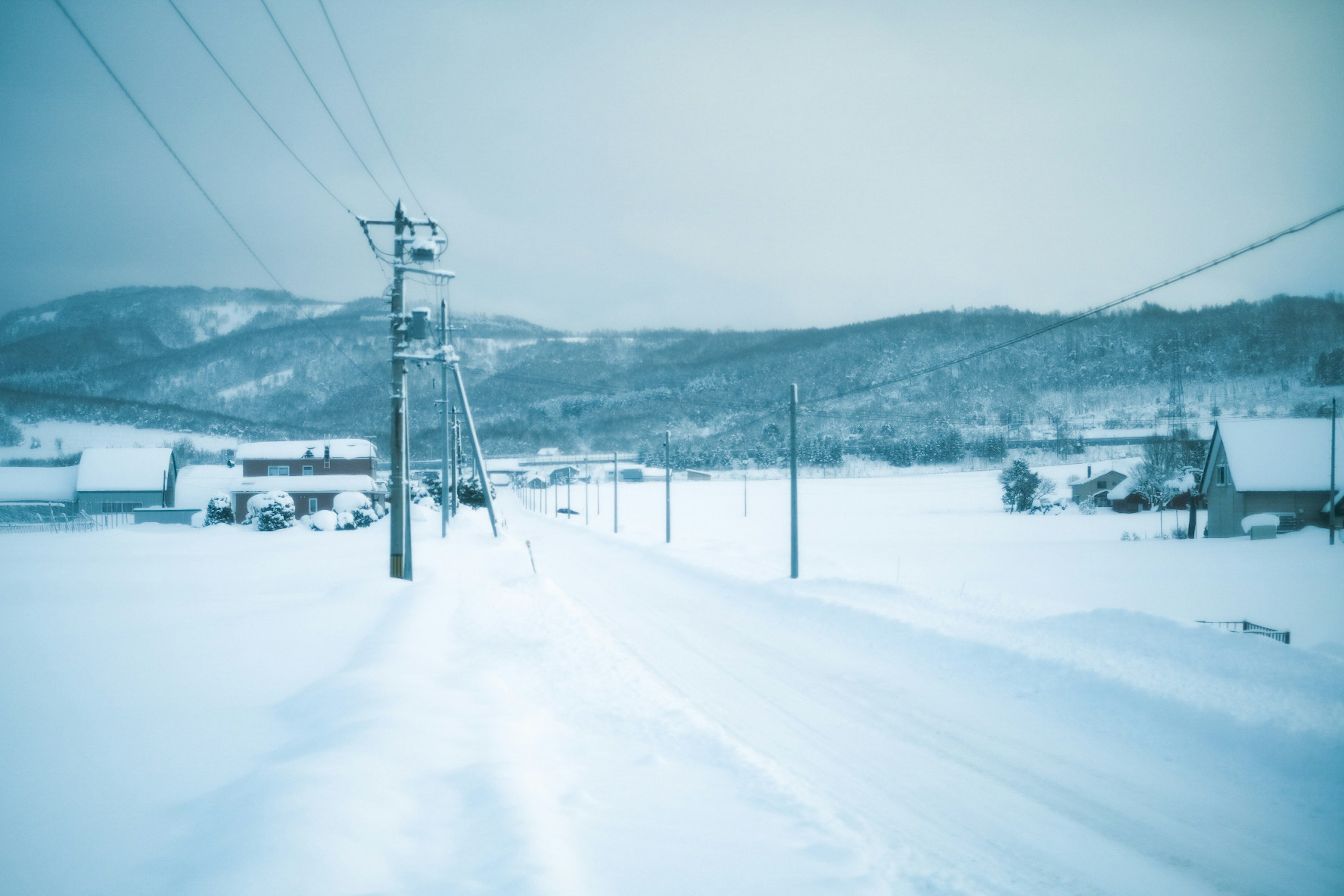 Schneebedeckte Straße mit Stromleitungen und fernen Hügeln