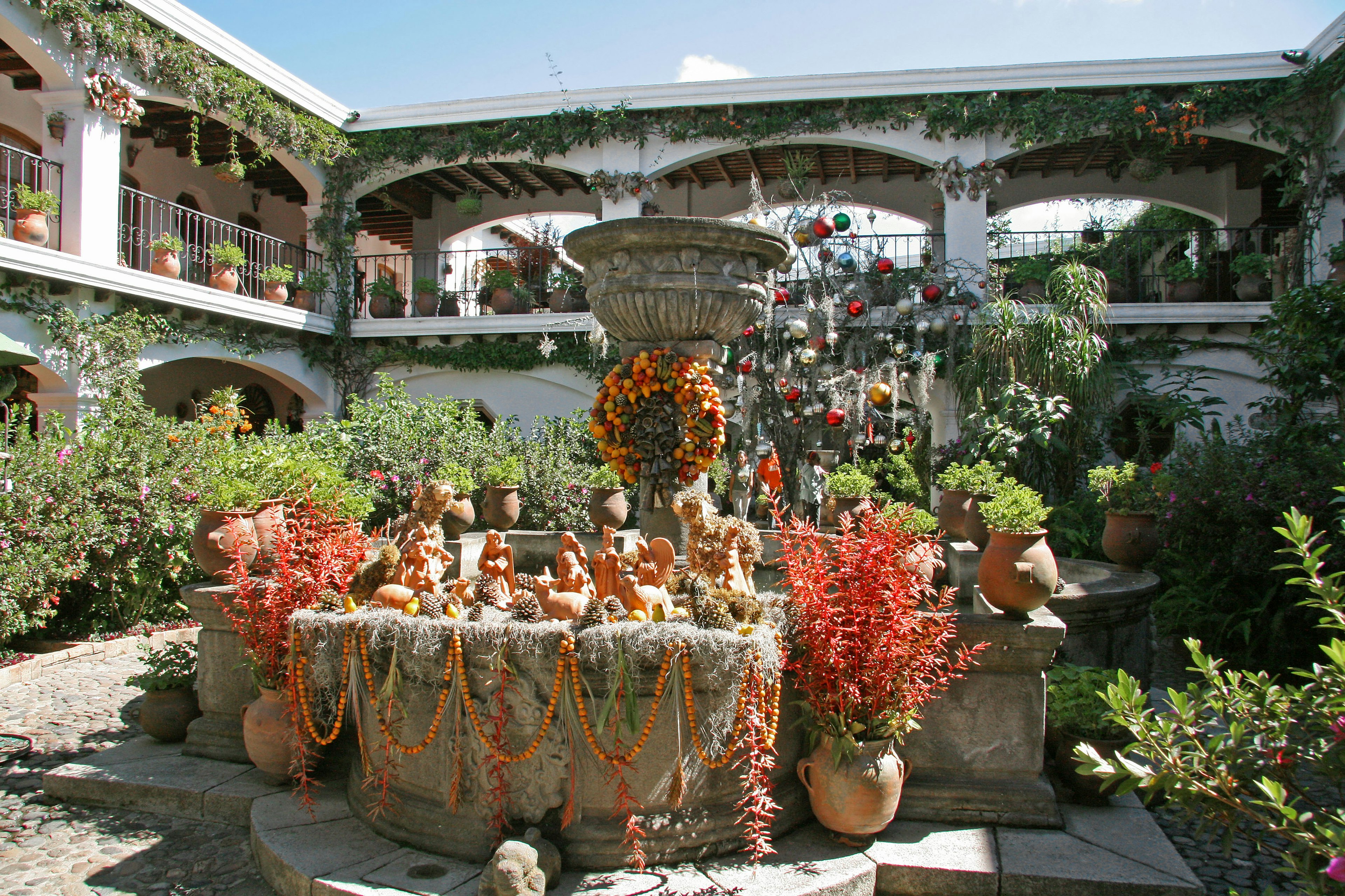 Cortile pittoresco con fontana circondata da piante colorate e vasi