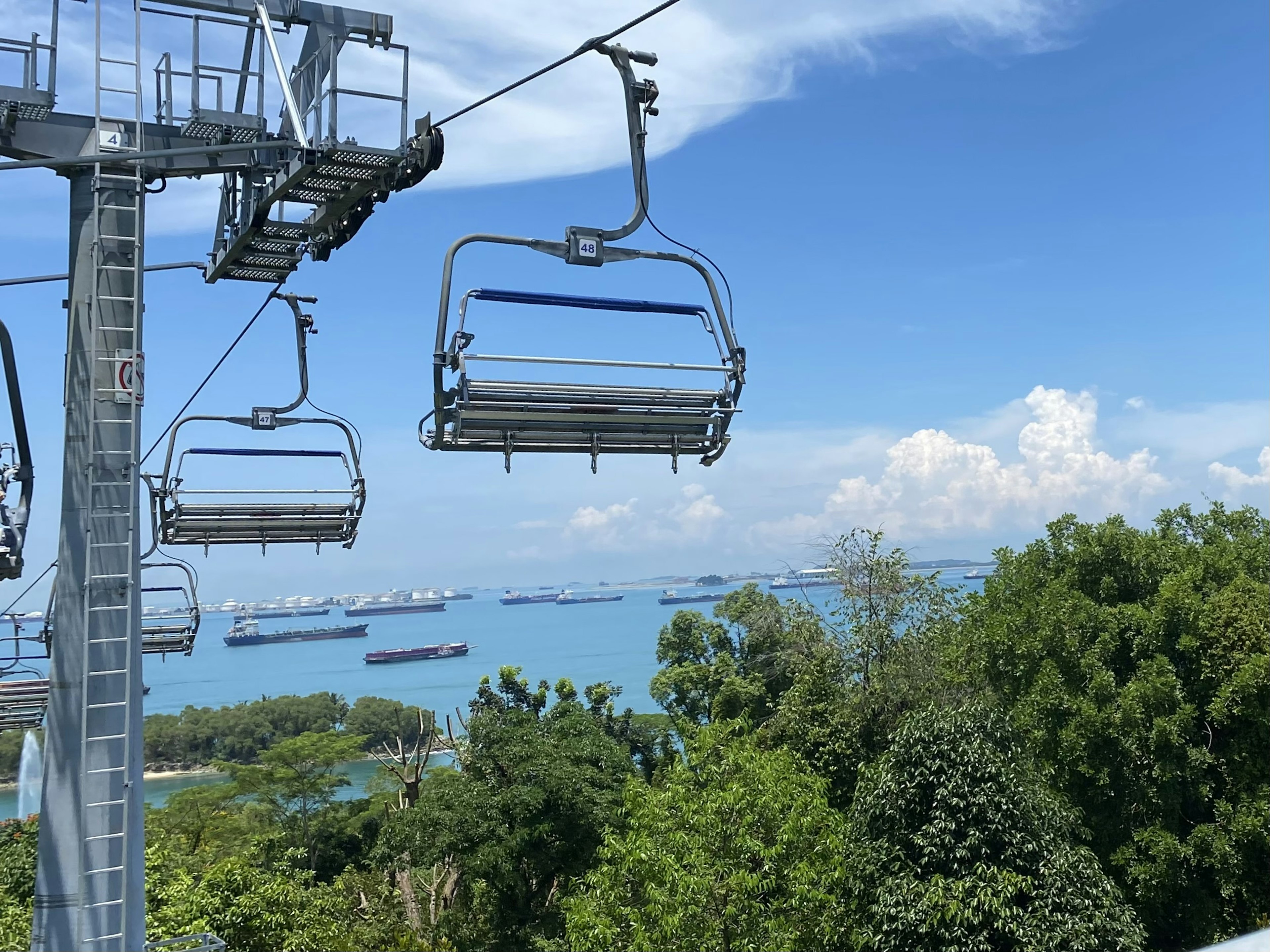 Teleférico con vista al mar azul árboles verdes y nubes blancas