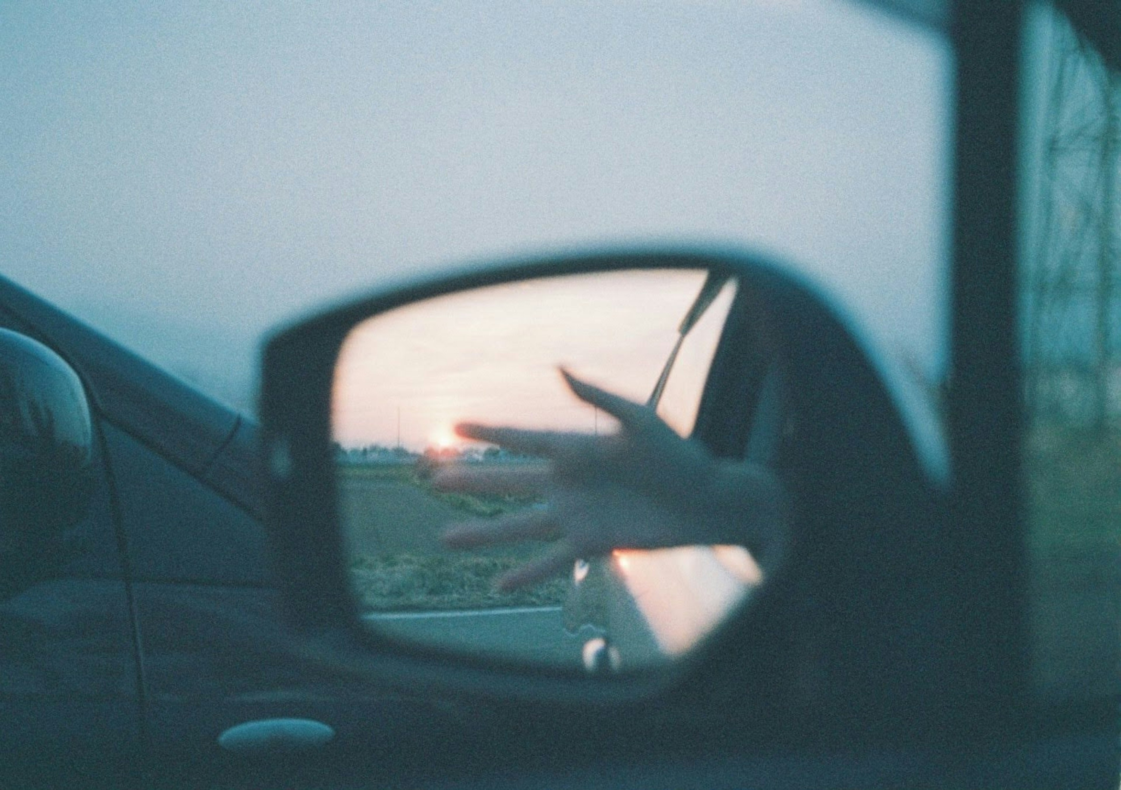 Reflejo del atardecer y silueta de mano en el espejo lateral del coche