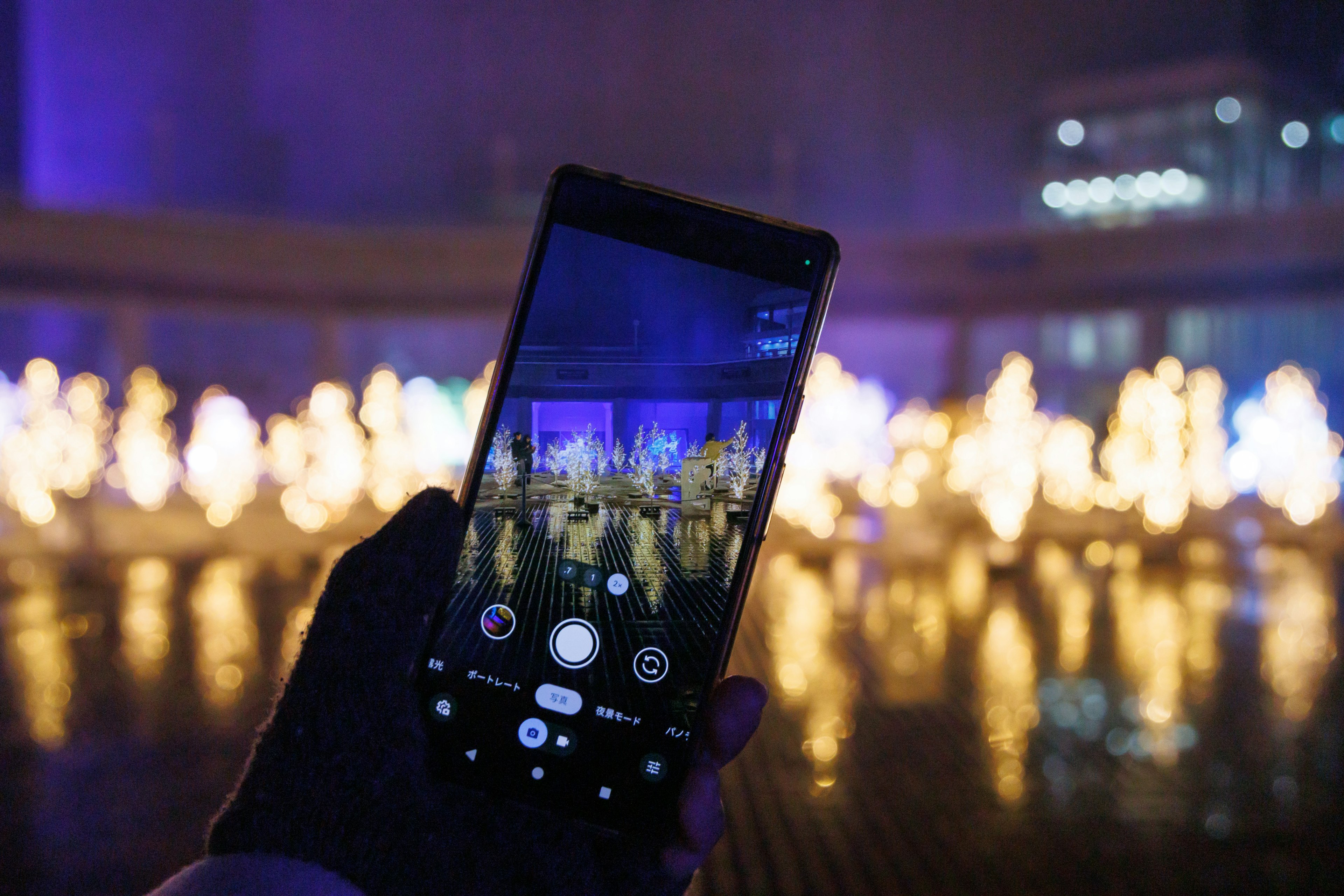 Un teléfono inteligente sostenido en una mano capturando un espectáculo de fuentes por la noche