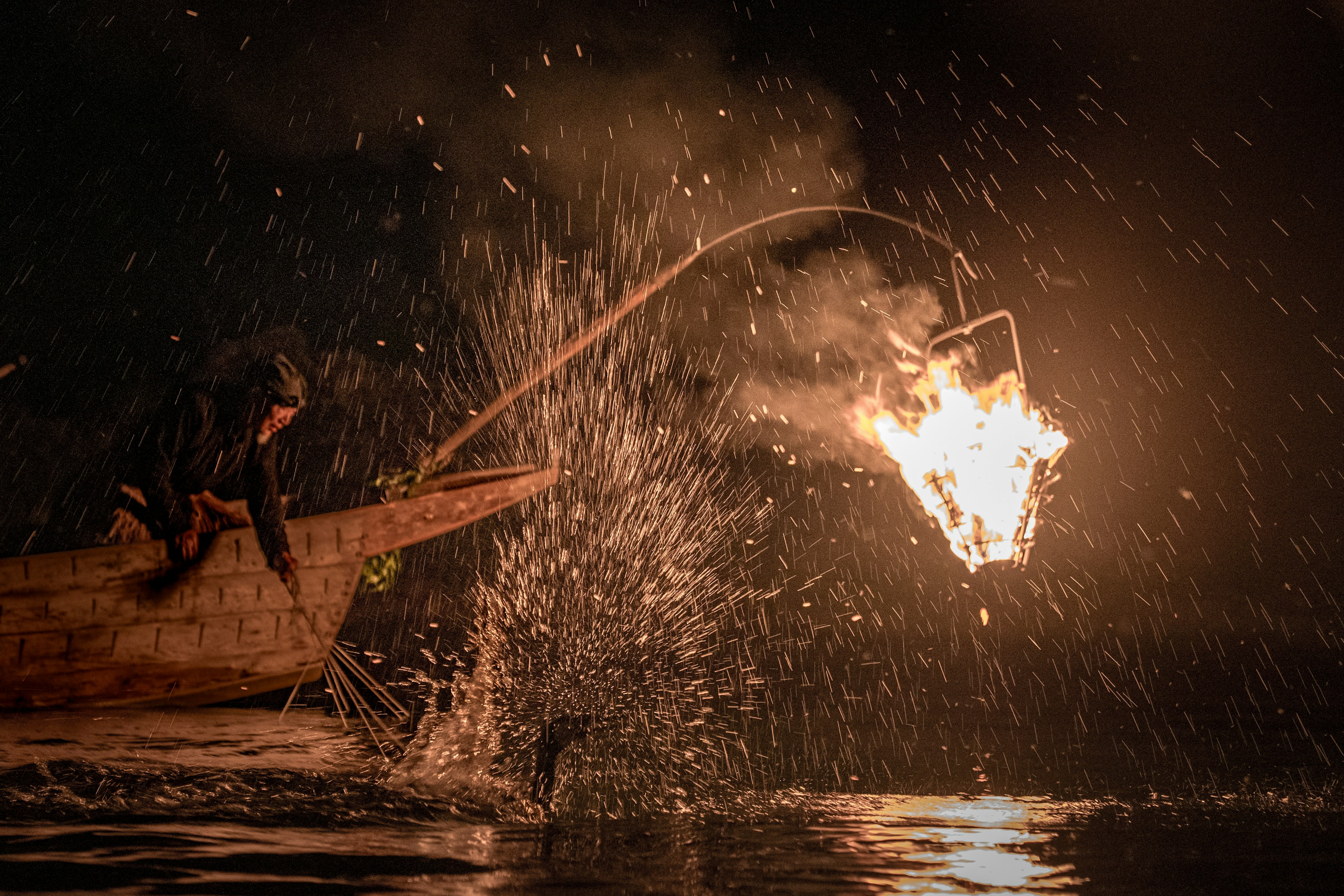 Fisherman in a small boat at night throwing a flaming object into the water