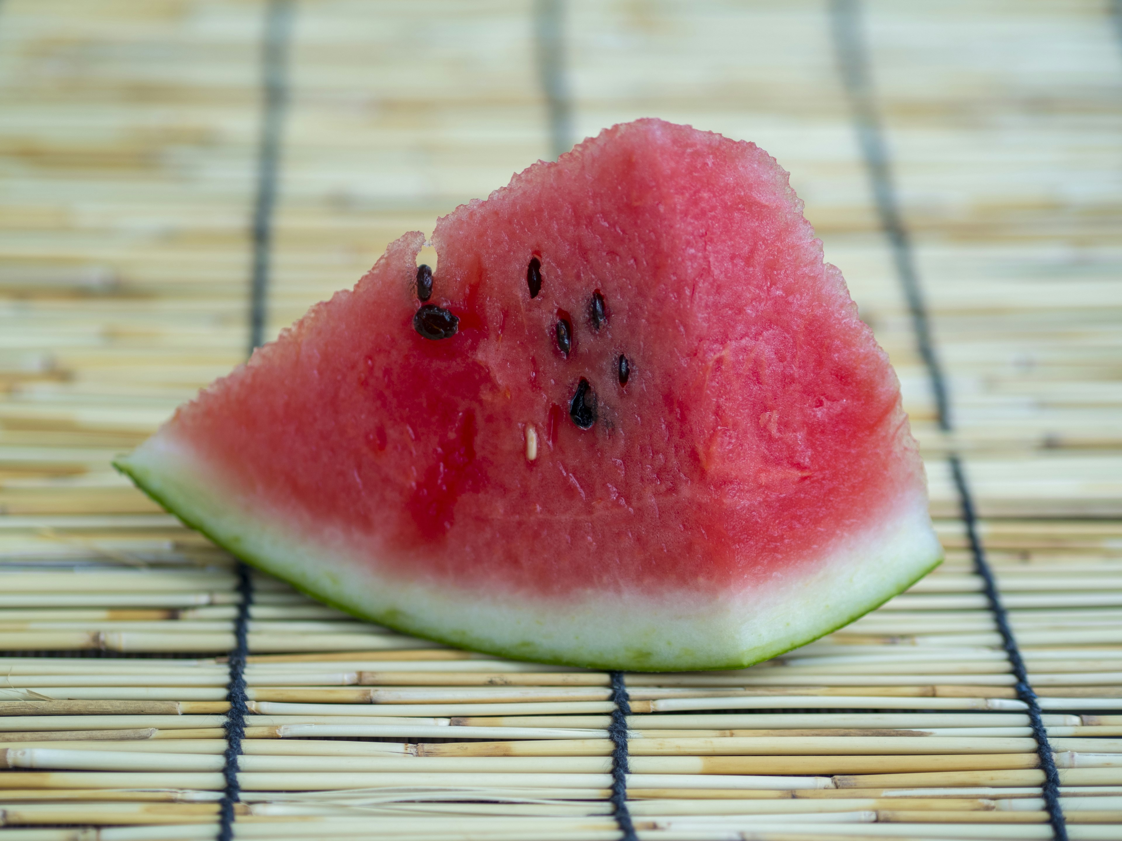 A slice of watermelon resting on a bamboo mat