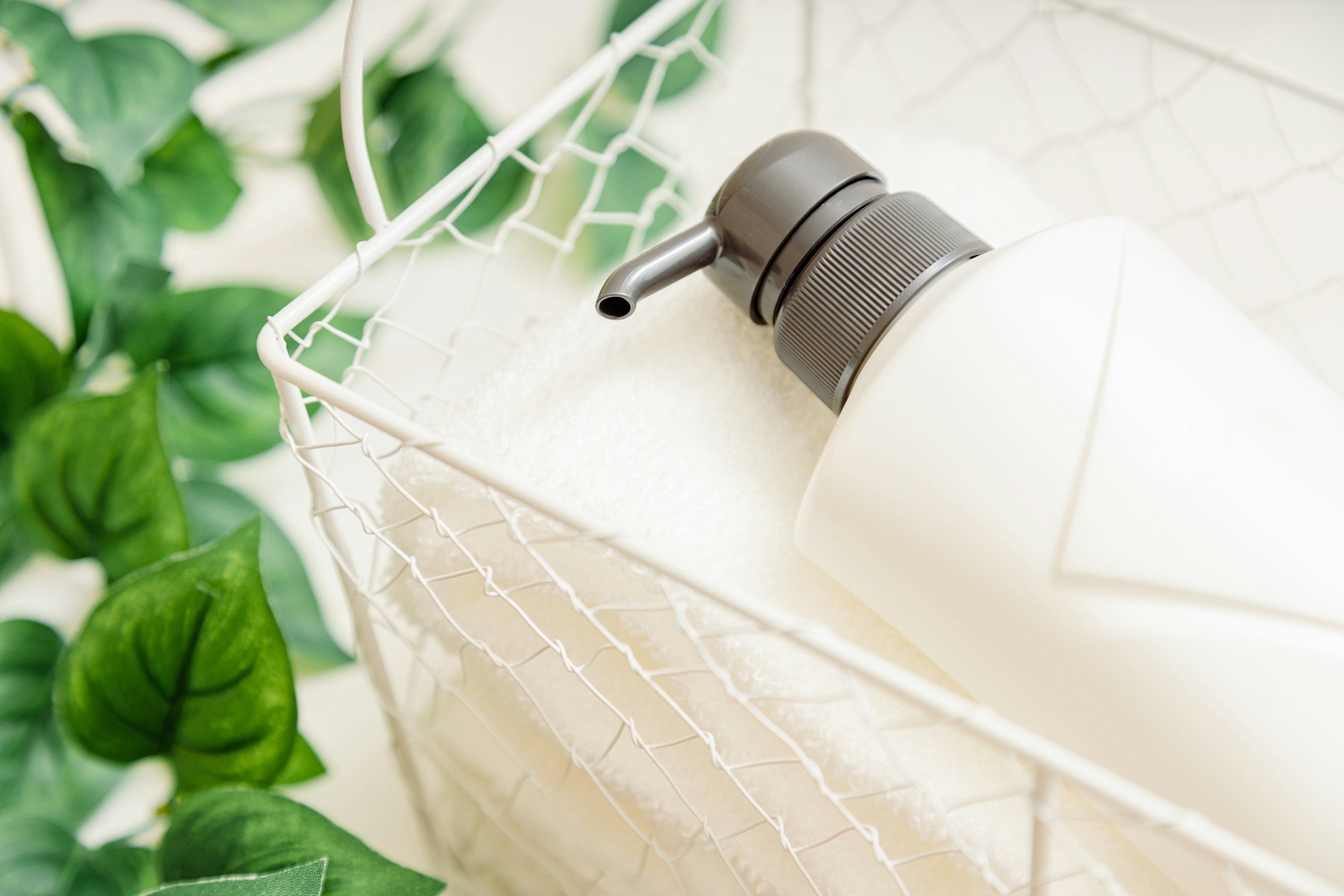 White bottle and towels in a wire basket with green leaves