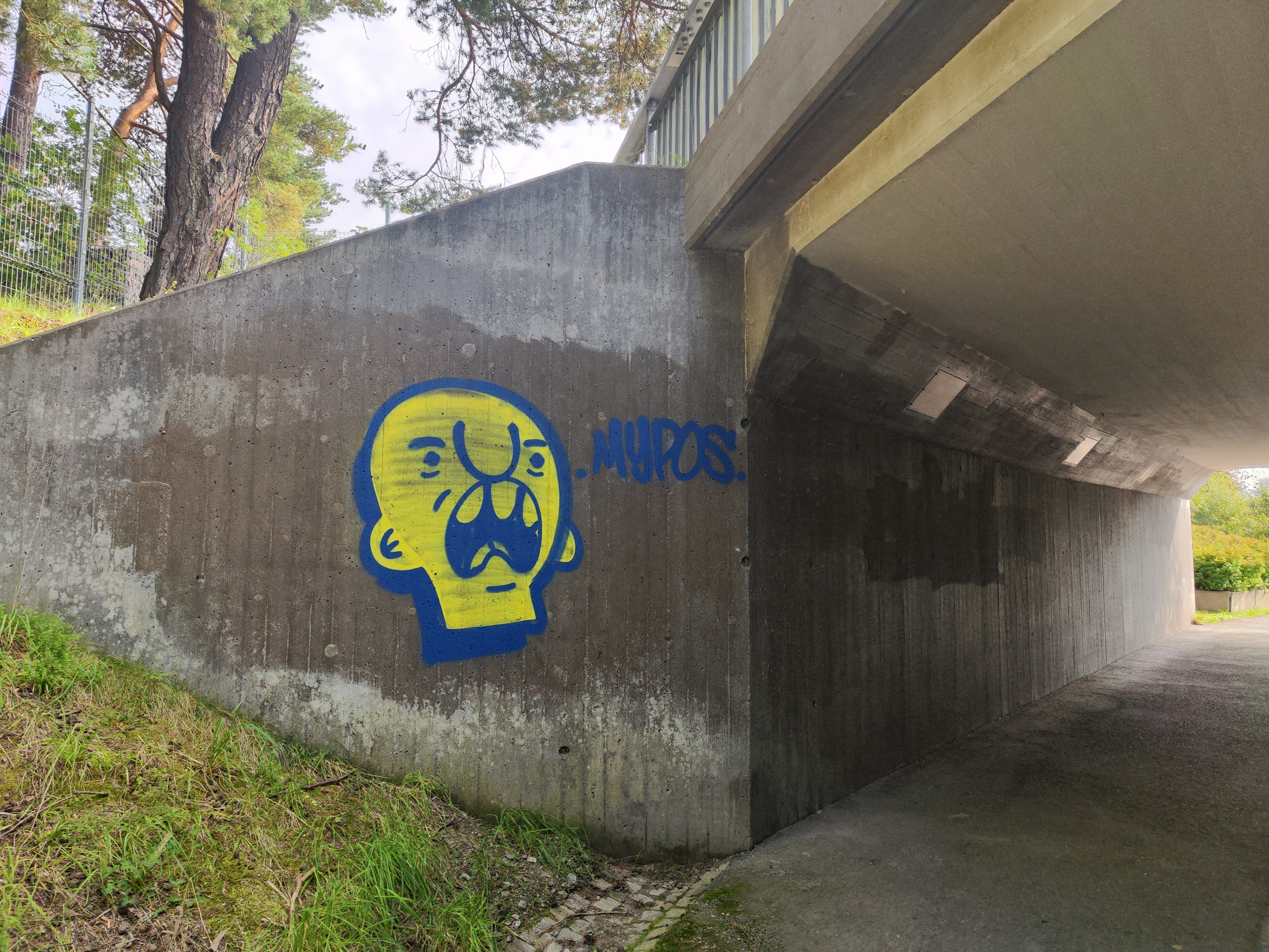 Graffiti amarillo vibrante de una cara expresiva bajo un puente