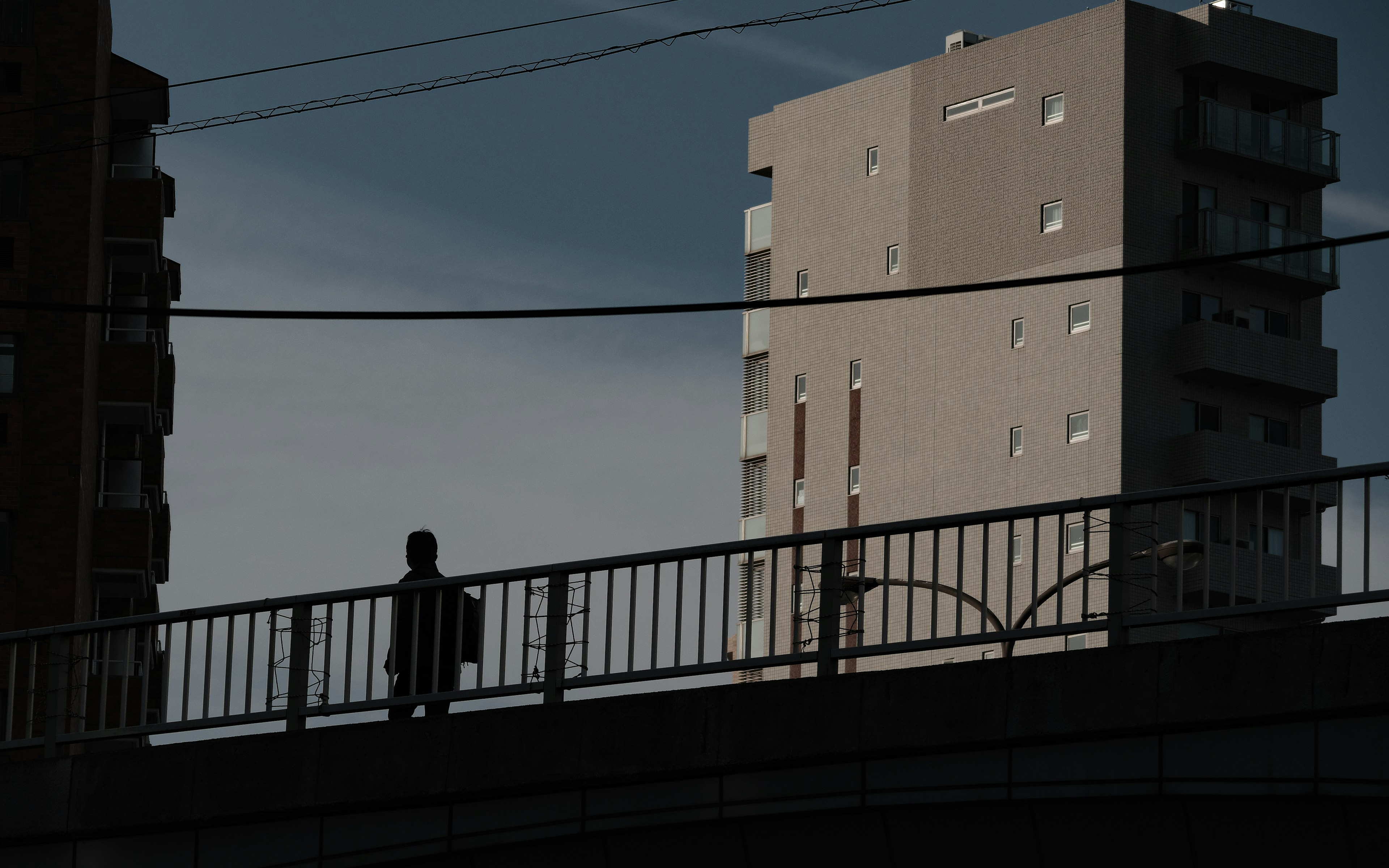 Silhouette of a person standing on a bridge with high-rise buildings in the background