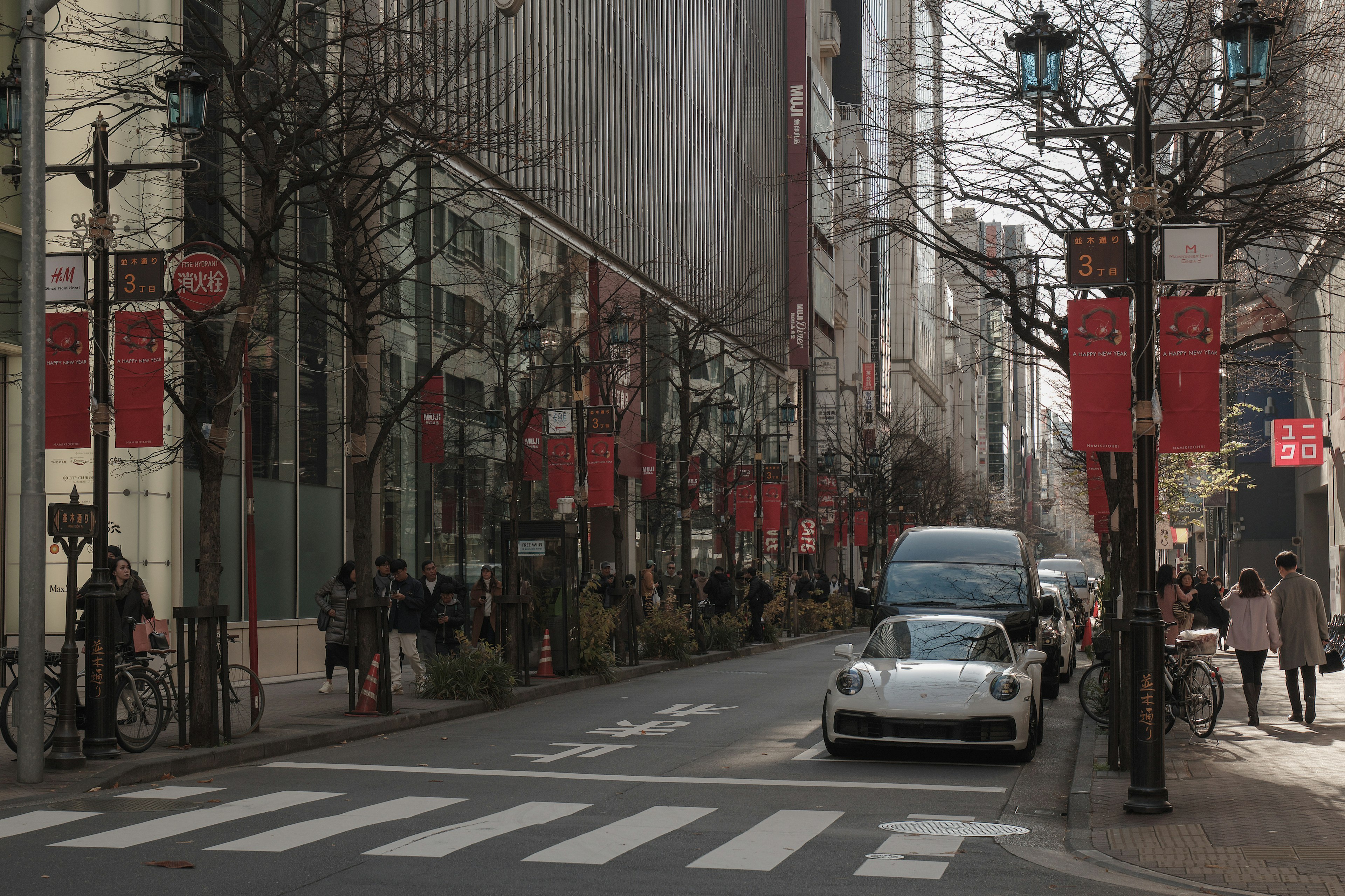 Silver car parked on a busy street with pedestrians and banners