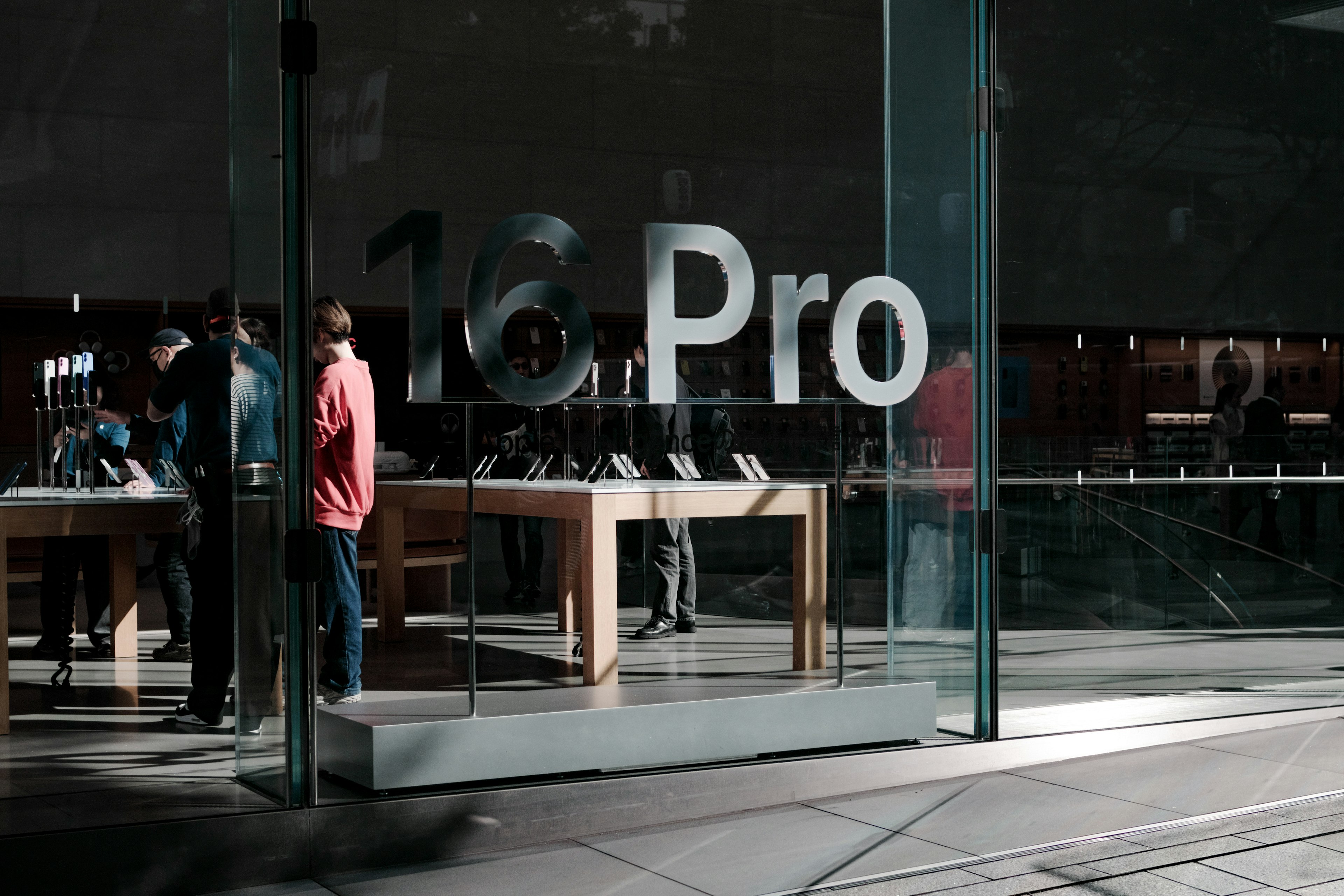 Entrée d'un Apple Store avec '16 Pro' sur la vitre et des clients parcourant les produits