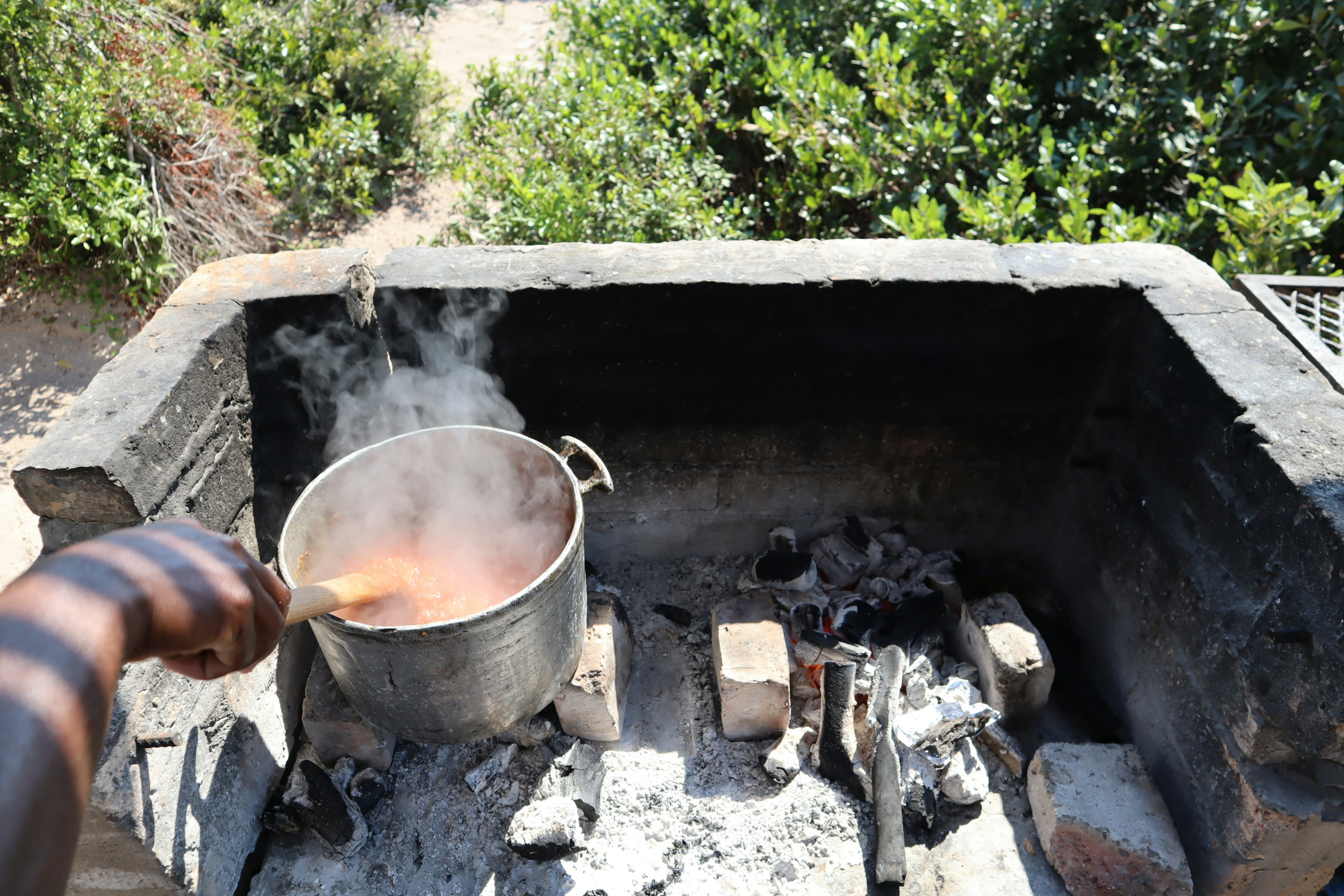 Scene of stirring a pot over an outdoor fire with rising smoke