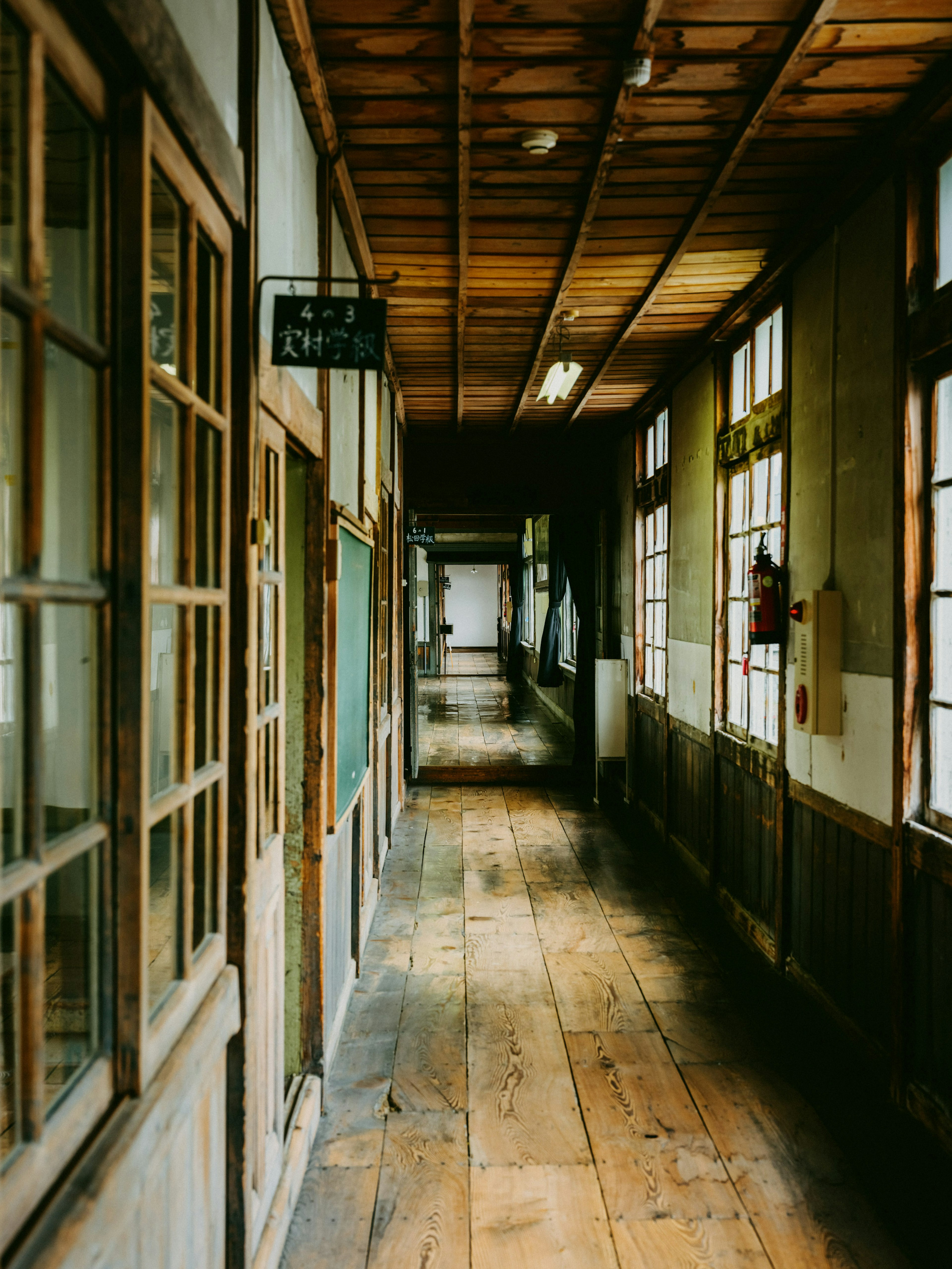 Lorong sekolah tua dengan lantai kayu dan dinding berpanel jendela