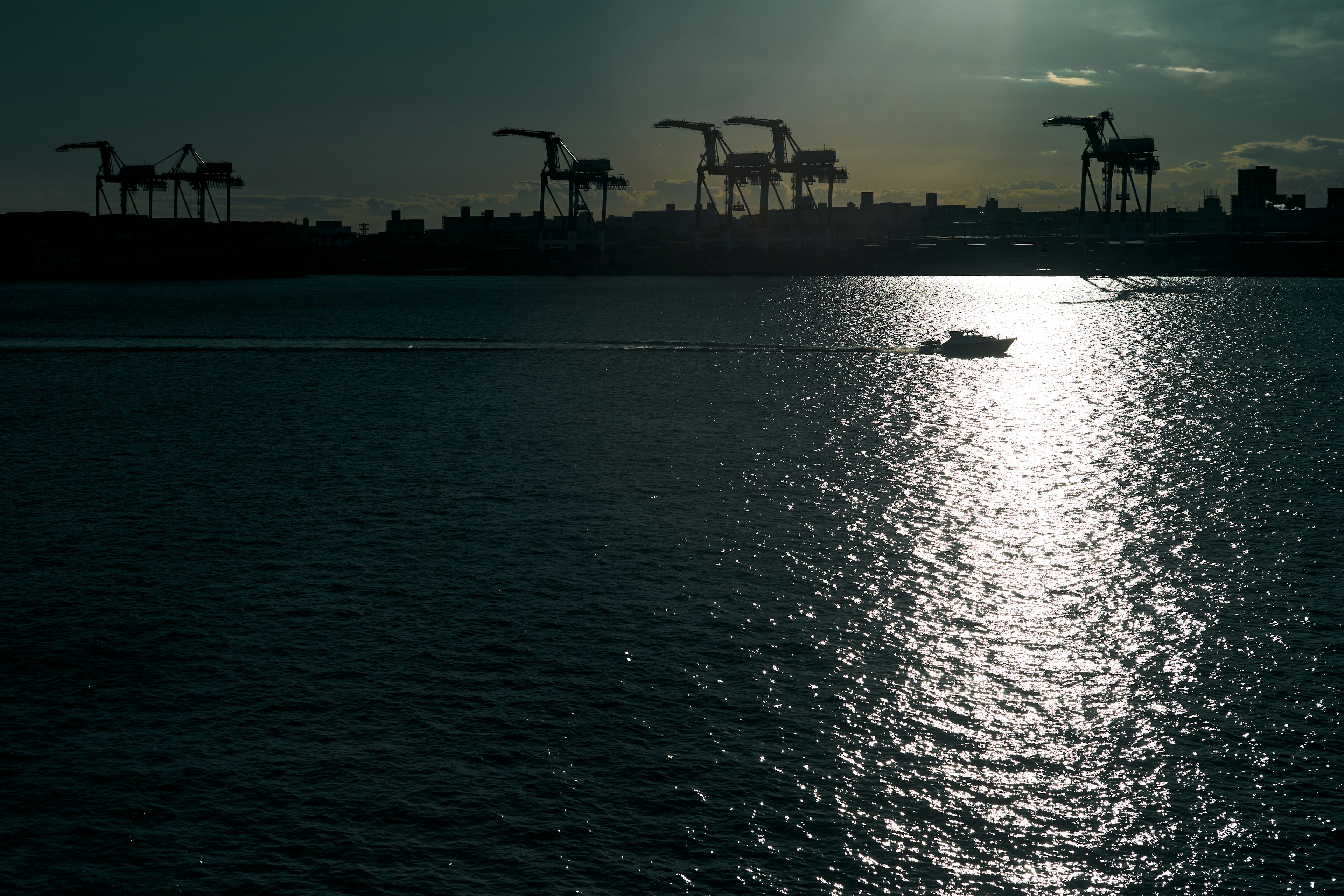 A boat on the water with silhouetted cranes in the background