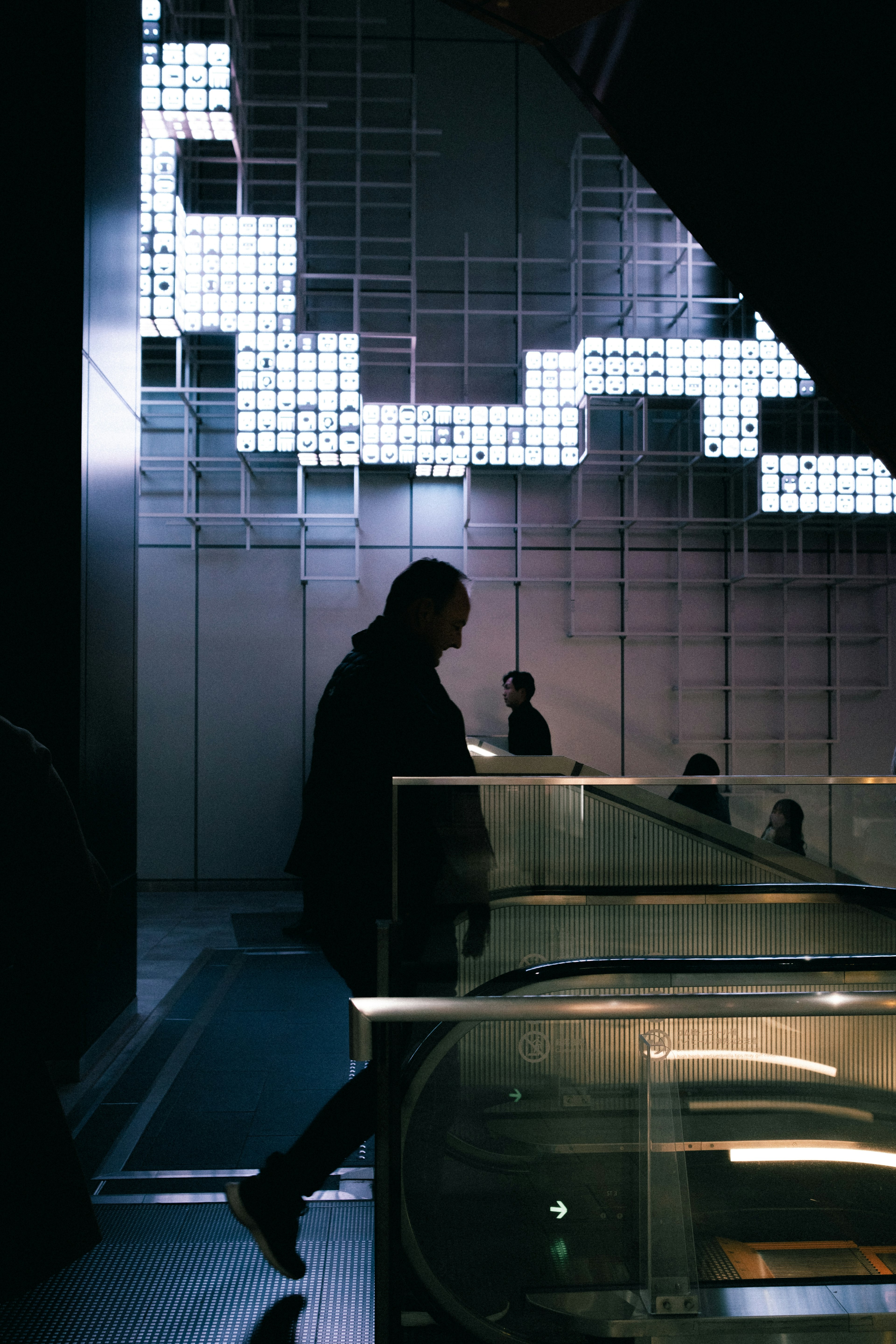 Silhouette d'une personne descendant des escaliers dans un espace moderne avec un mur géométrique lumineux