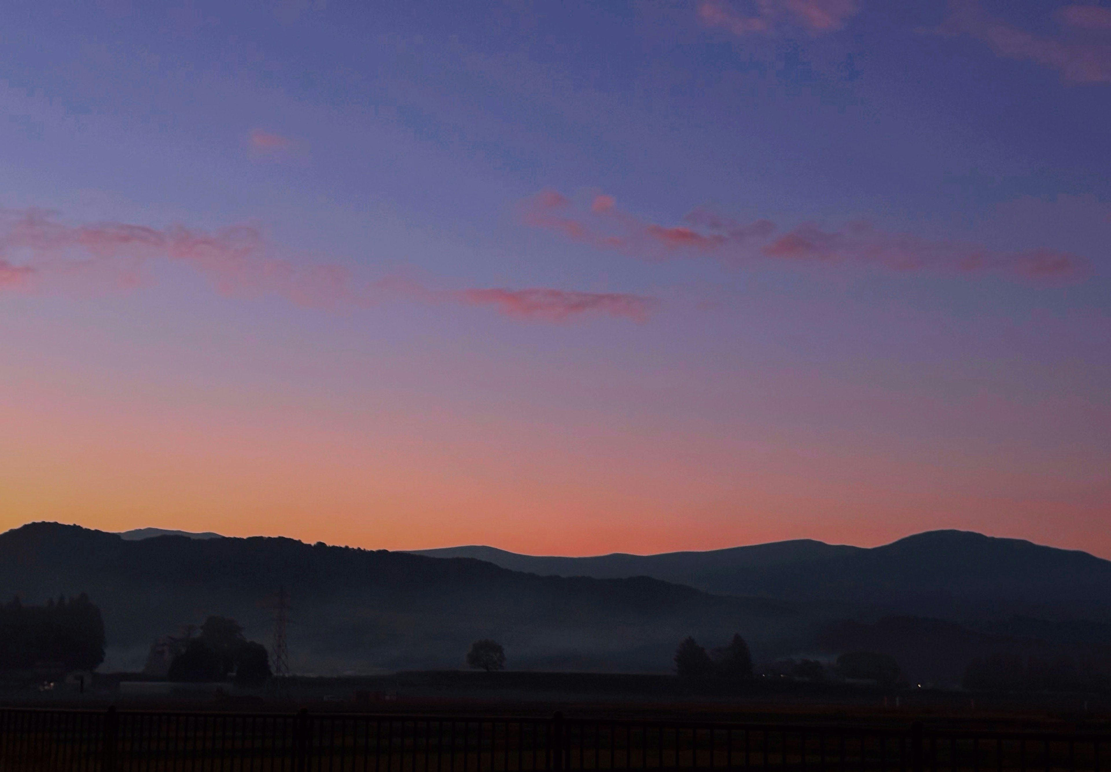 Hermoso paisaje del amanecer con montañas y llanuras brumosas, cielo azul-púrpura con nubes rosas