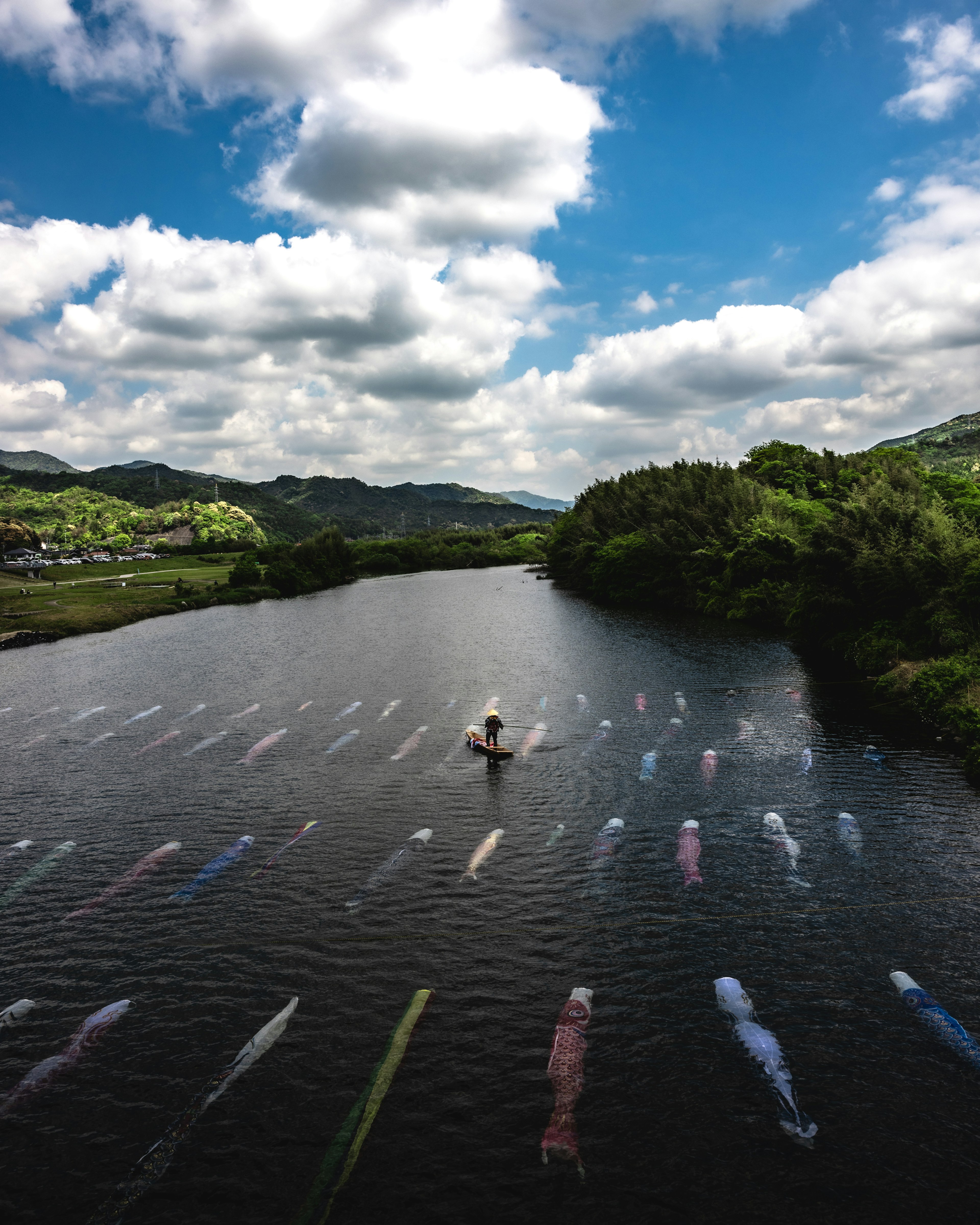 Person rowing on a river under blue sky and white clouds with colorful flags