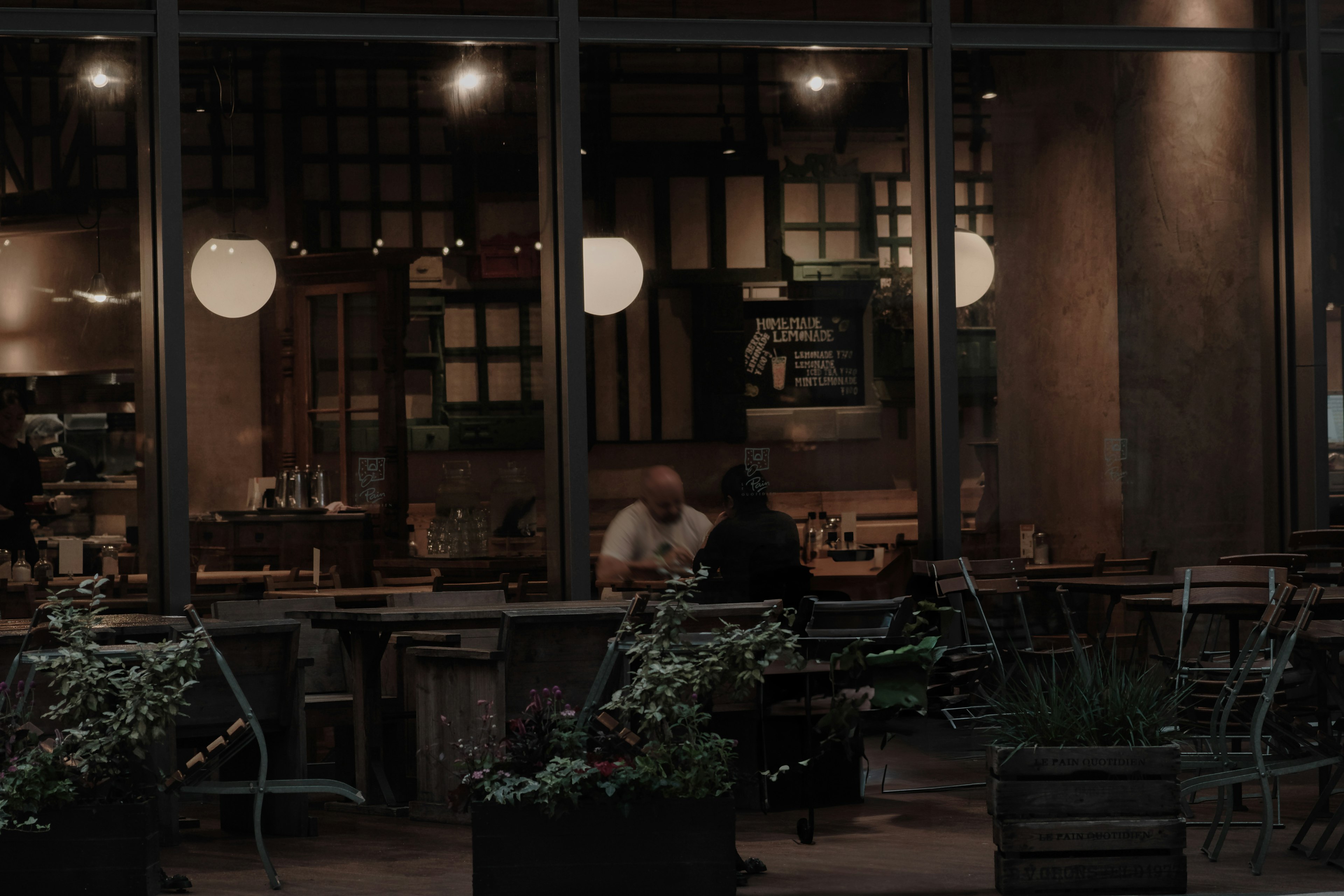 Cozy café interior visible through large windows with two patrons and greenery