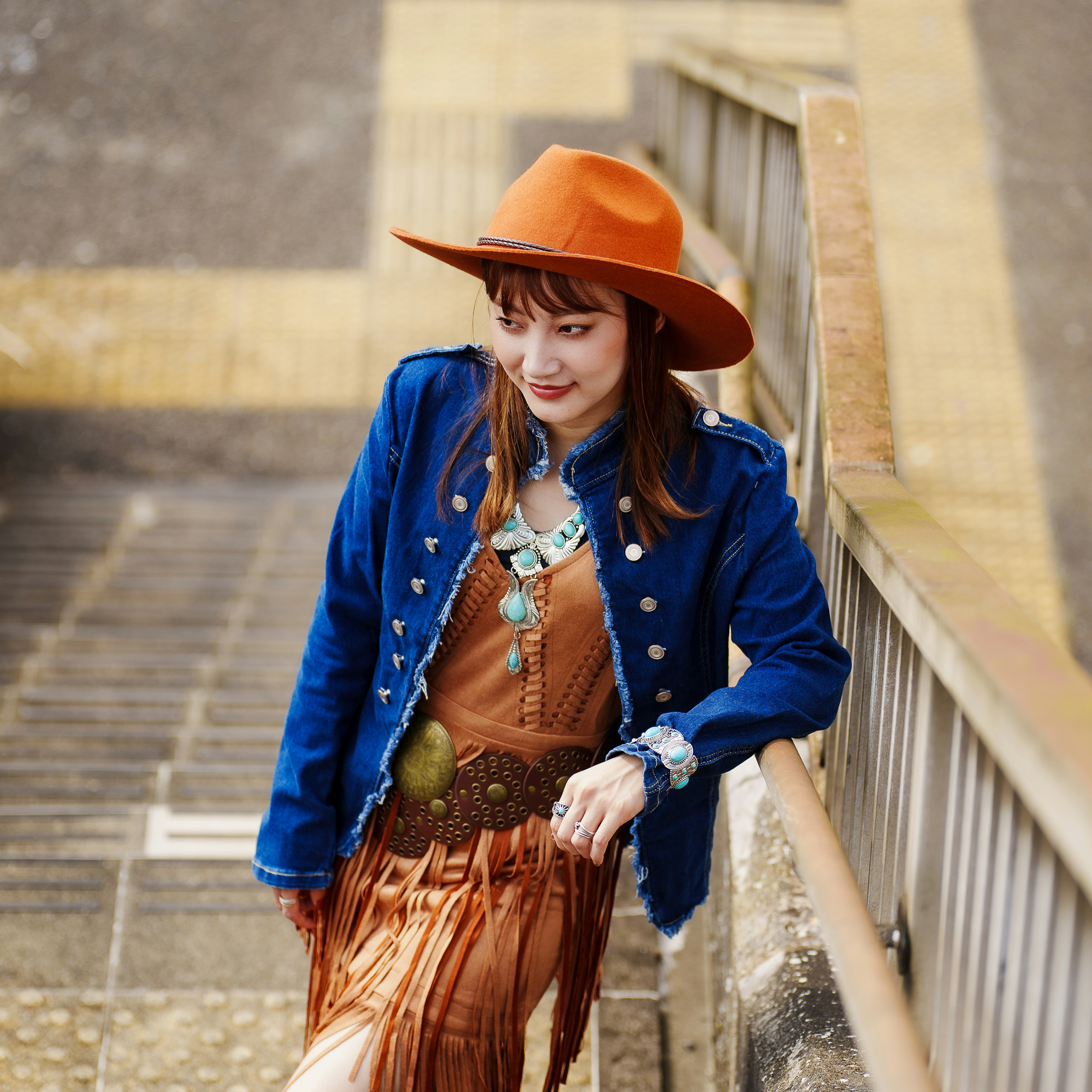 Frau in blauer Jacke und orangefarbenem Hut, die auf Treppen posiert