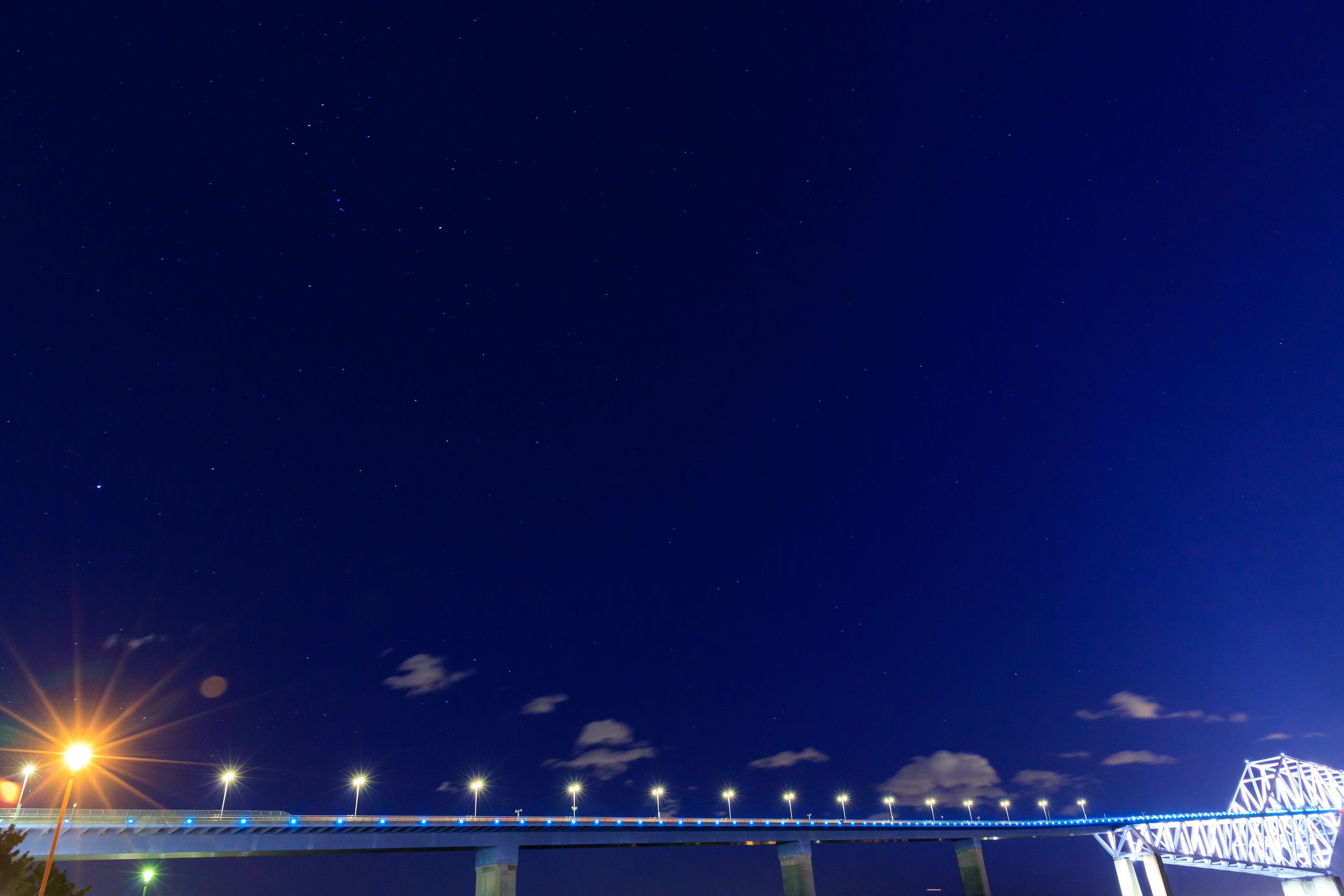 Night sky with stars and a bridge illuminated in blue lights