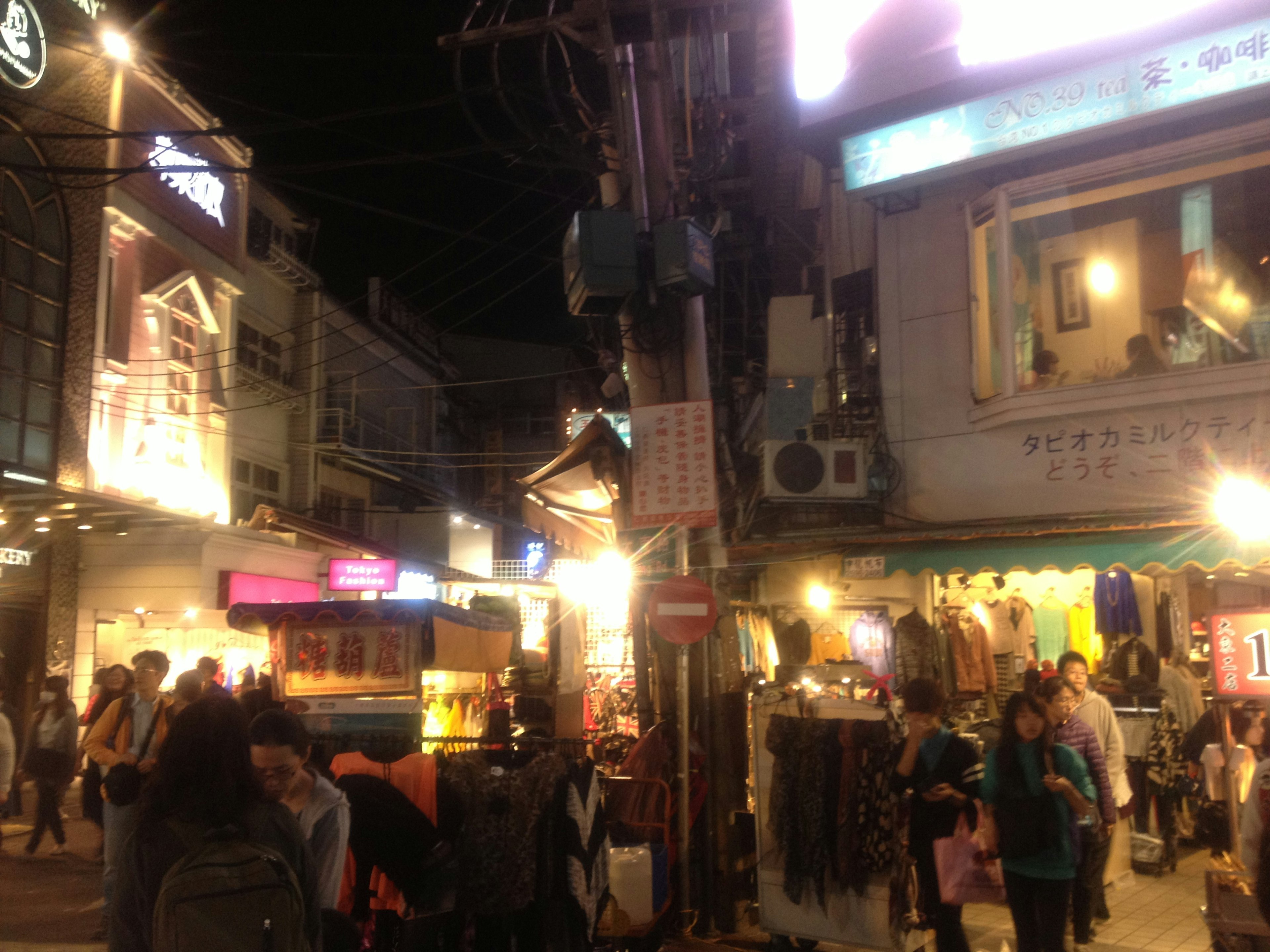 Busy street at night with people gathering and various shops lining the way