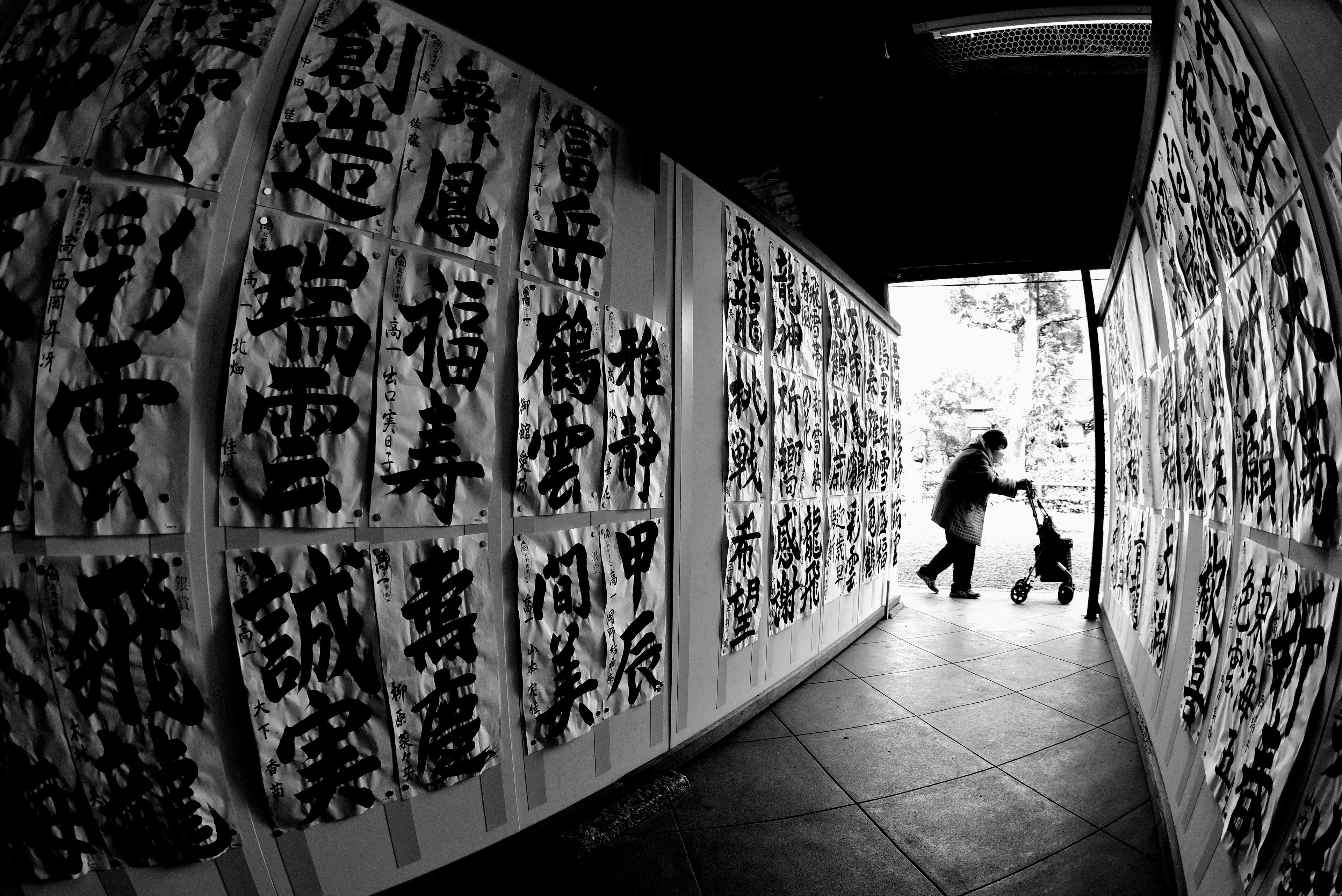 Pasillo en blanco y negro lleno de obras de caligrafía con una persona y un niño de fondo