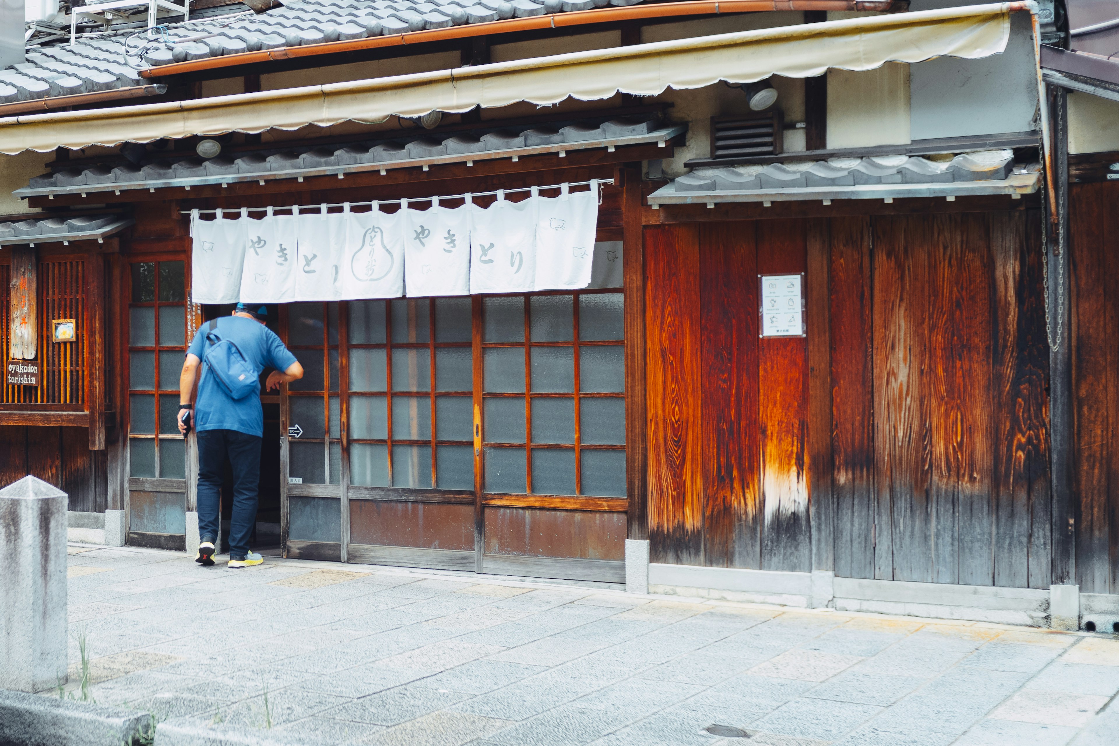 Exterior de una casa japonesa tradicional con puerta de madera y pared de color cálido, con un cortina noren blanca