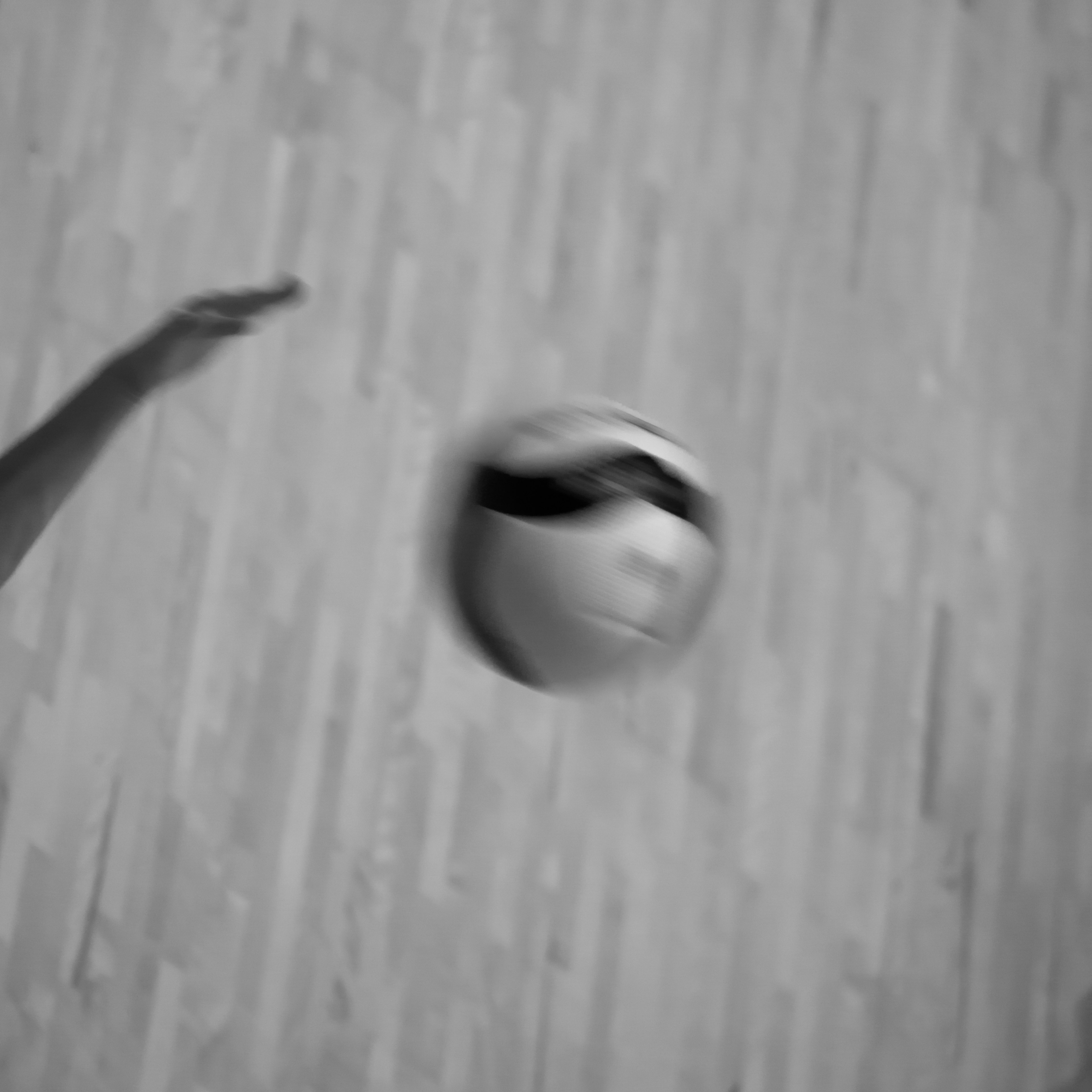 A hand reaching to throw a soccer ball with a wooden floor background