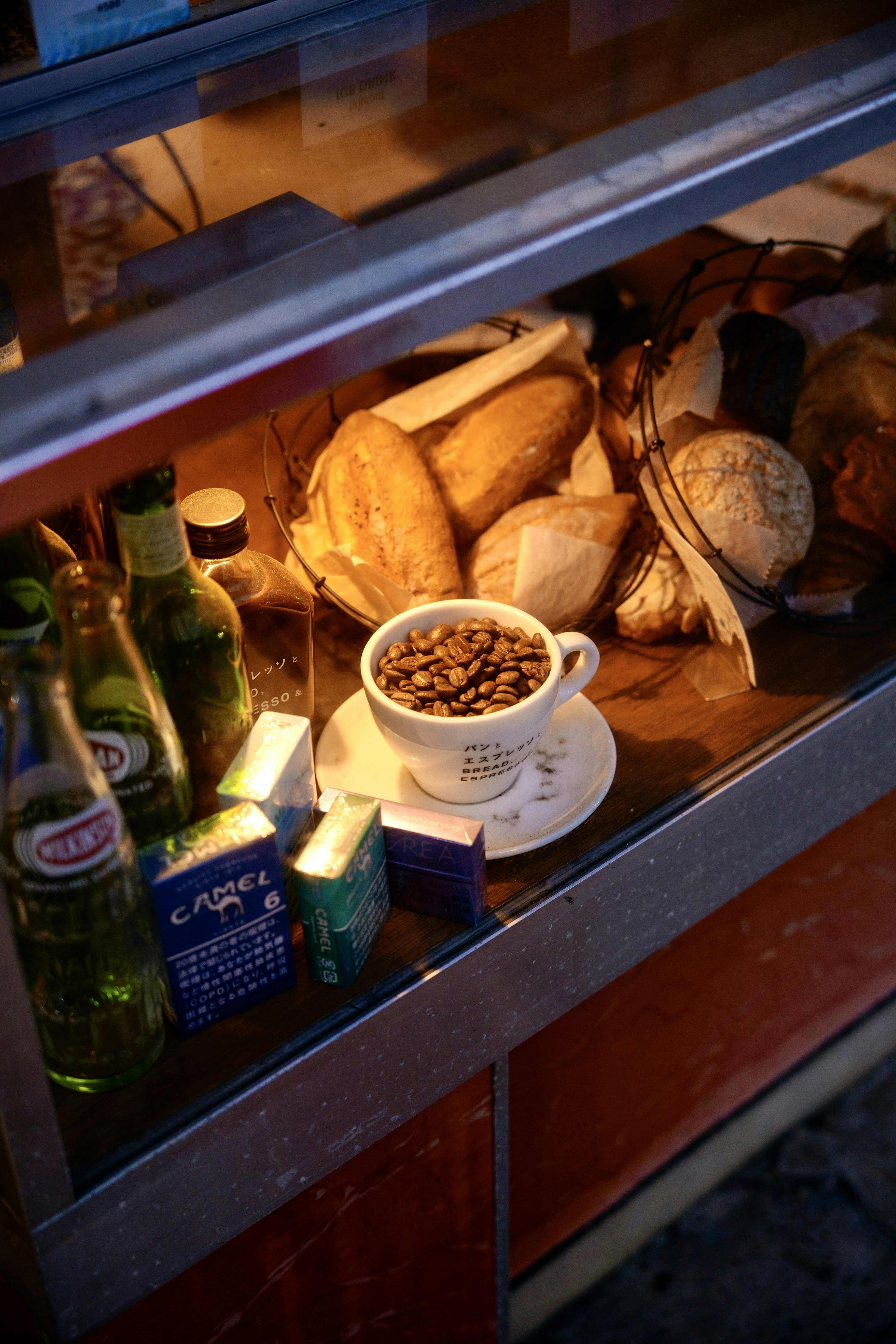 Coffee beans in a cup surrounded by various breads and beverages in a cafe display