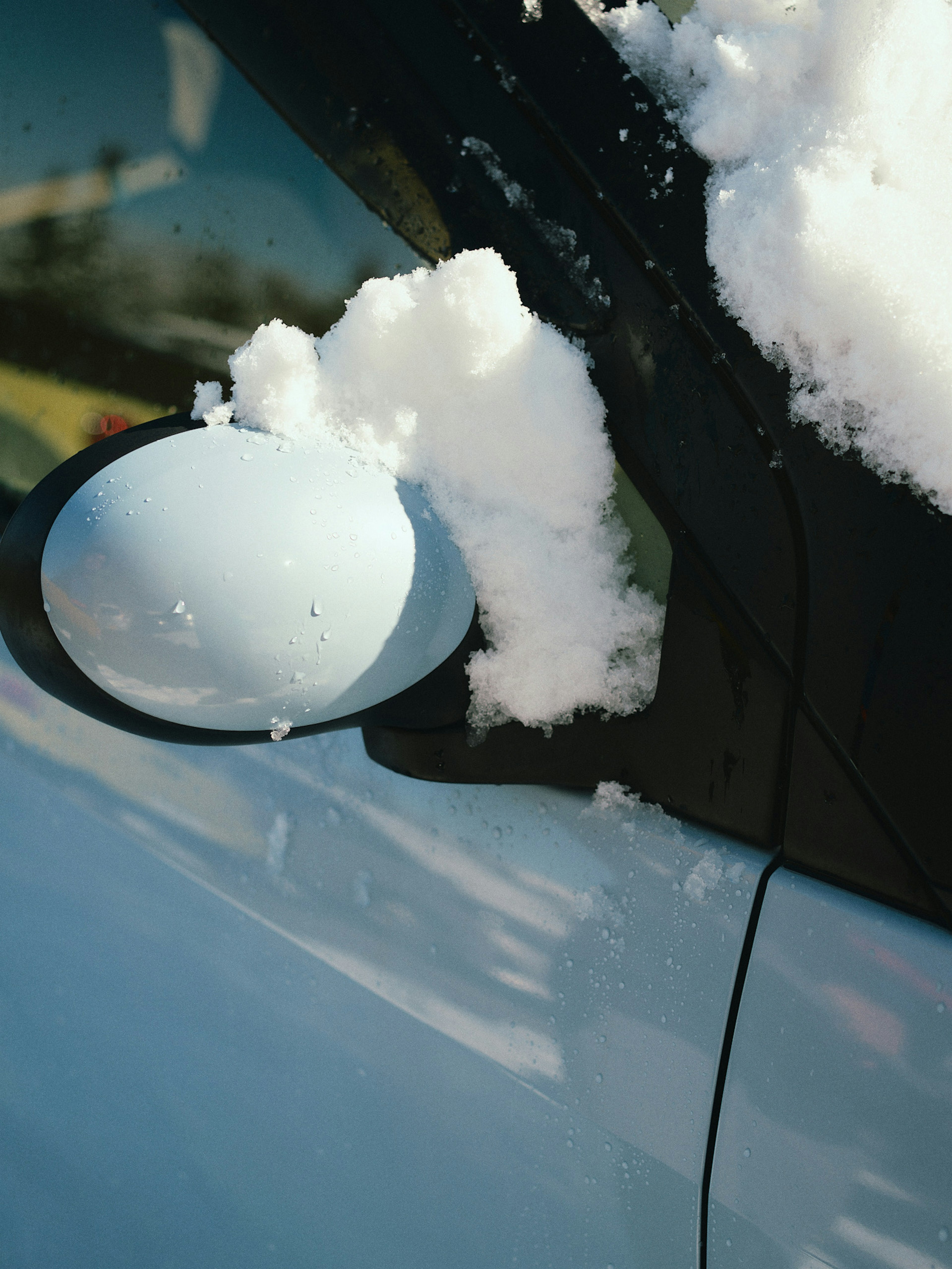 Close-up of a blue car's side mirror covered in snow