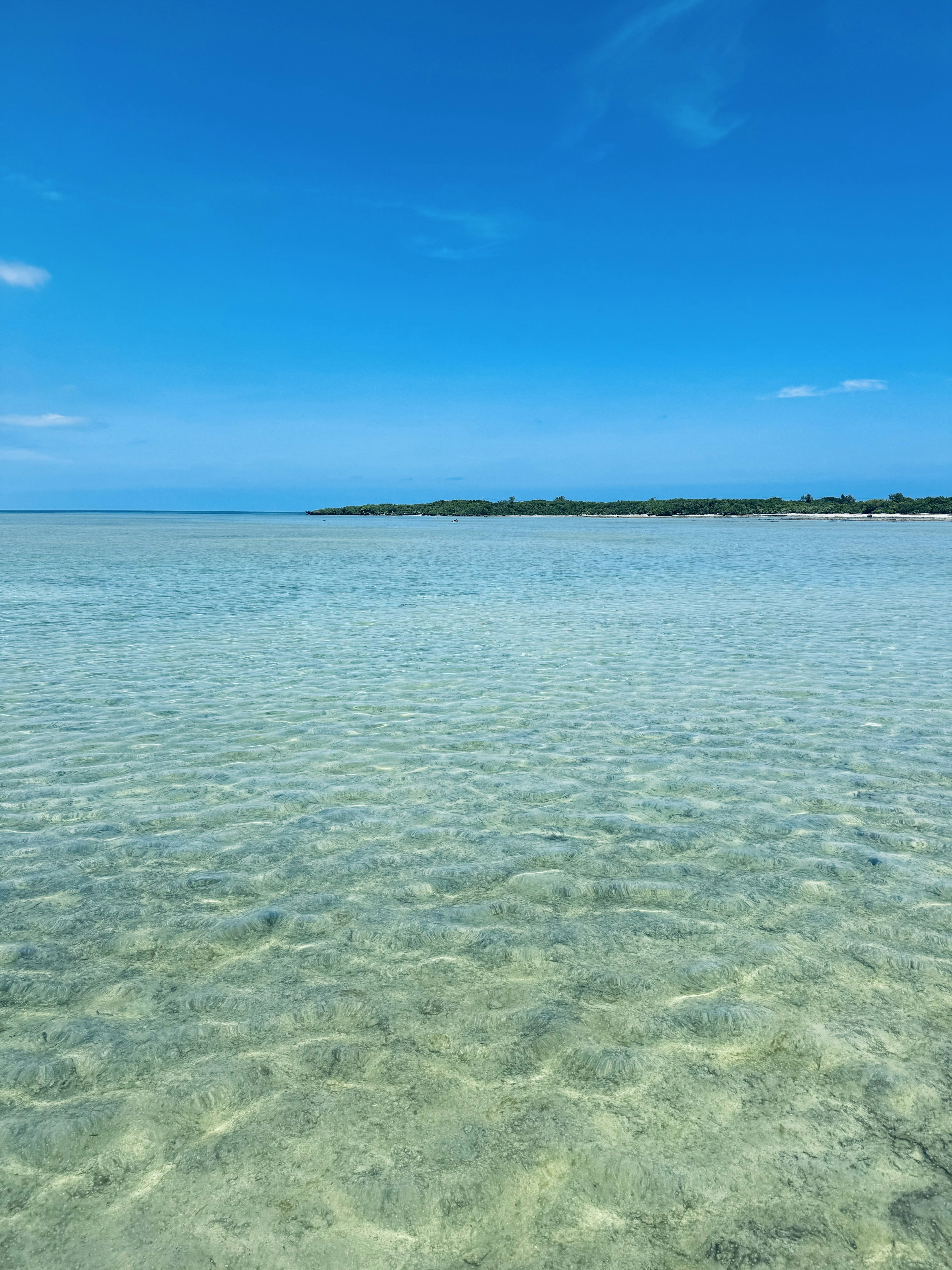 Agua turquesa clara con un cielo azul brillante y una costa lejana