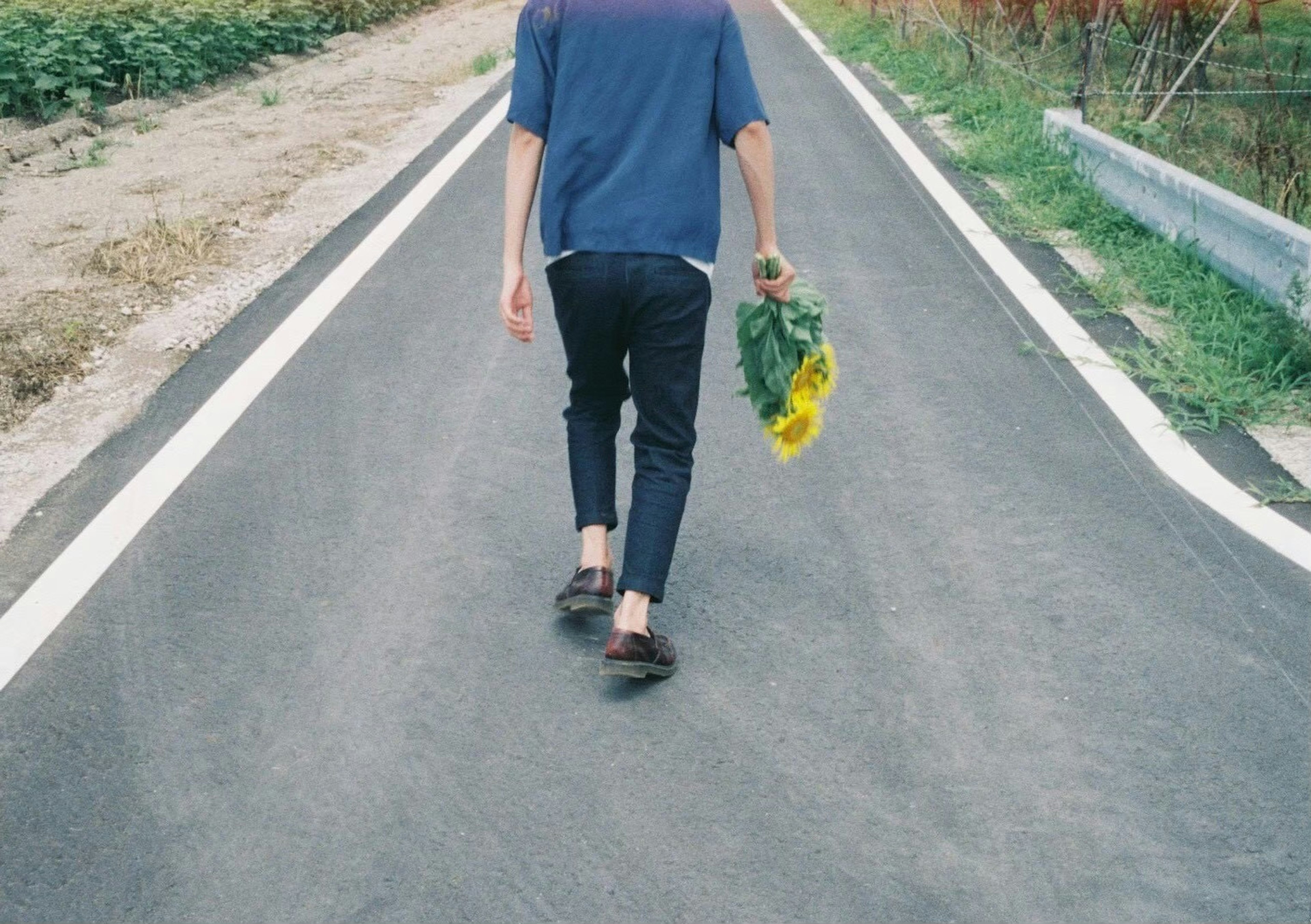 Personne marchant sur une route tenant des tournesols